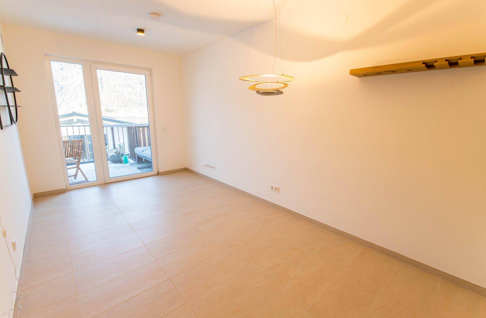 Geräumiges Wohnzimmer mit Zugang zum Balkon und hellen Bodenfliesen.