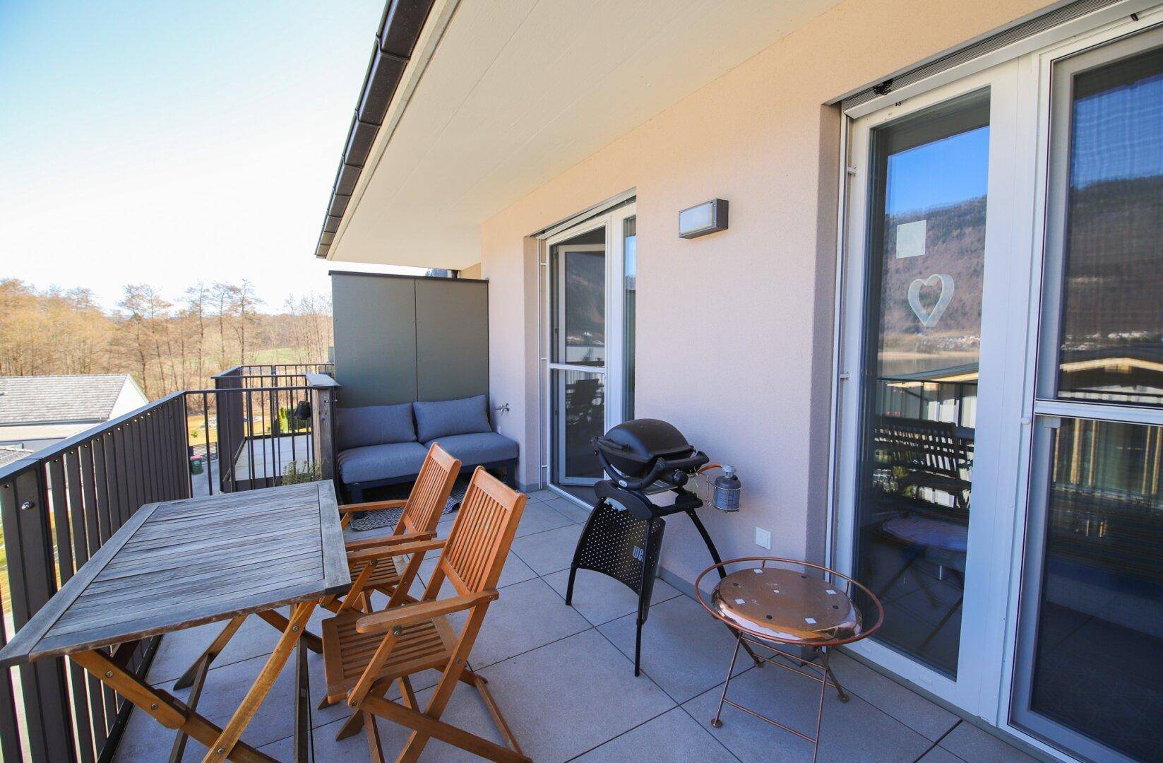 Sonniger Balkon mit Blick auf den See und die Berge, ausgestattet mit Tisch und Stühlen.