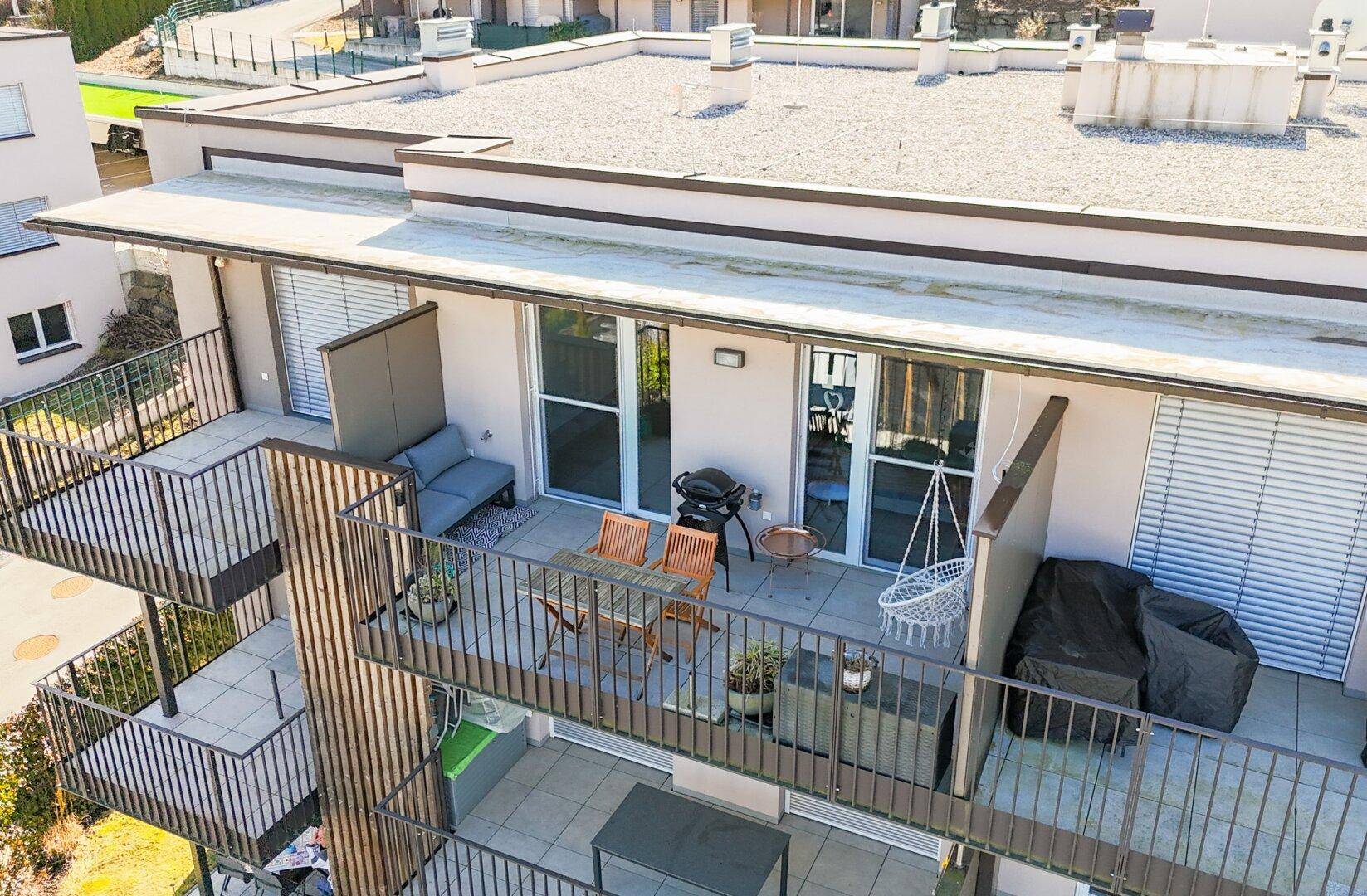 Großer Balkon mit Sitzgelegenheiten, Grill und Blick auf die bewaldeten Hügel.