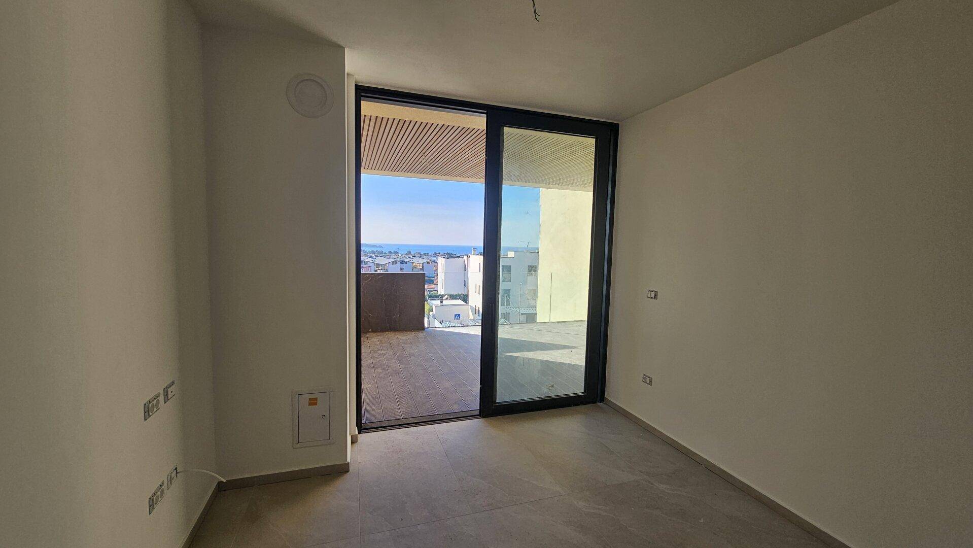 Heller, leerer Raum mit großen Schiebetüren zum Balkon und weitem Meerblick.