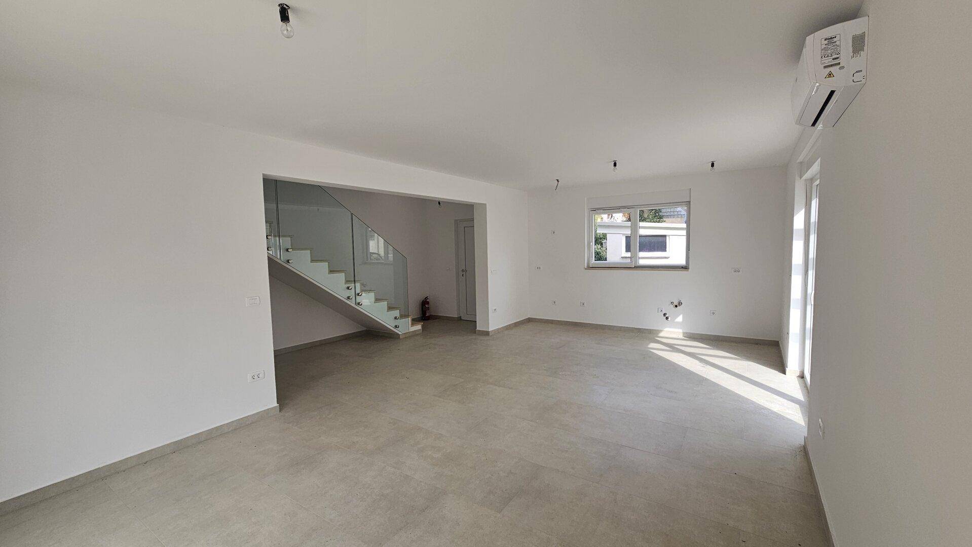 Heller Wohnbereich mit Fliesenboden, offener Treppe und viel natürlichem Licht.