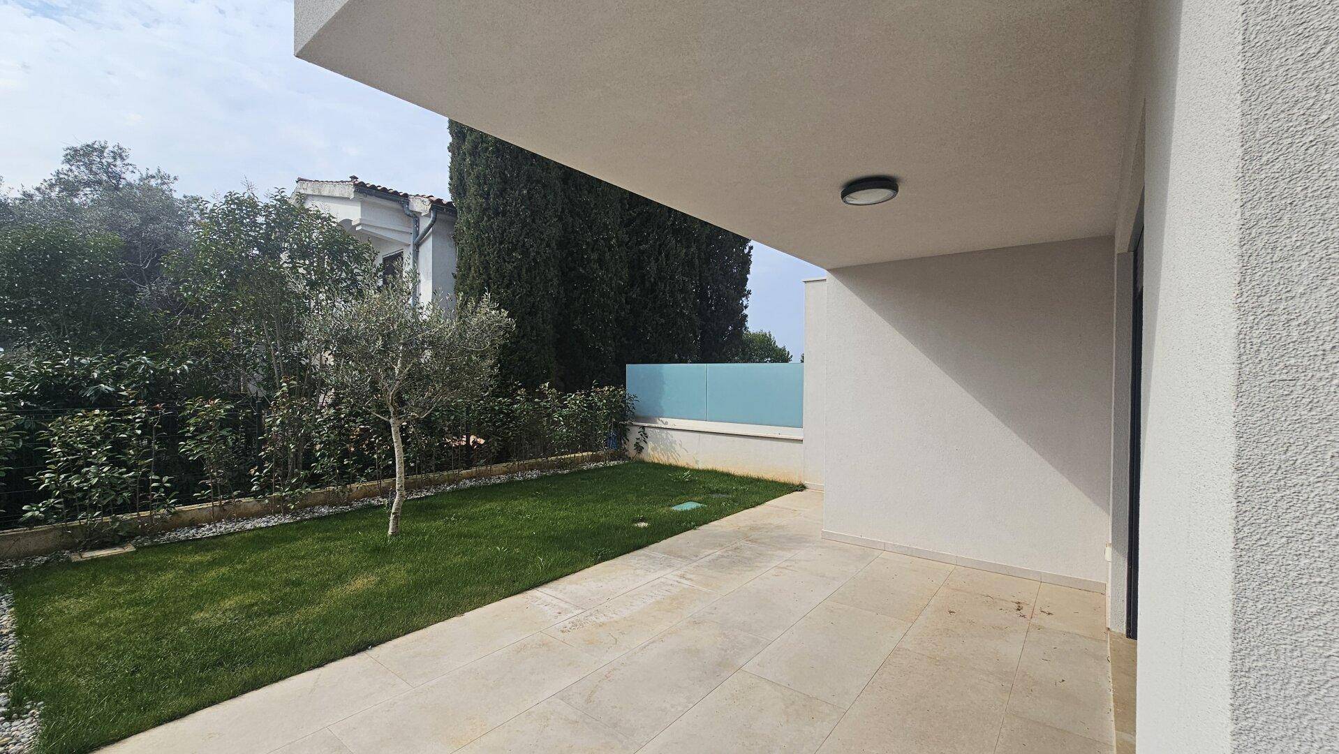 Private Terrasse mit gepflastertem Bereich, kleinem Rasen und grüner Hecke.