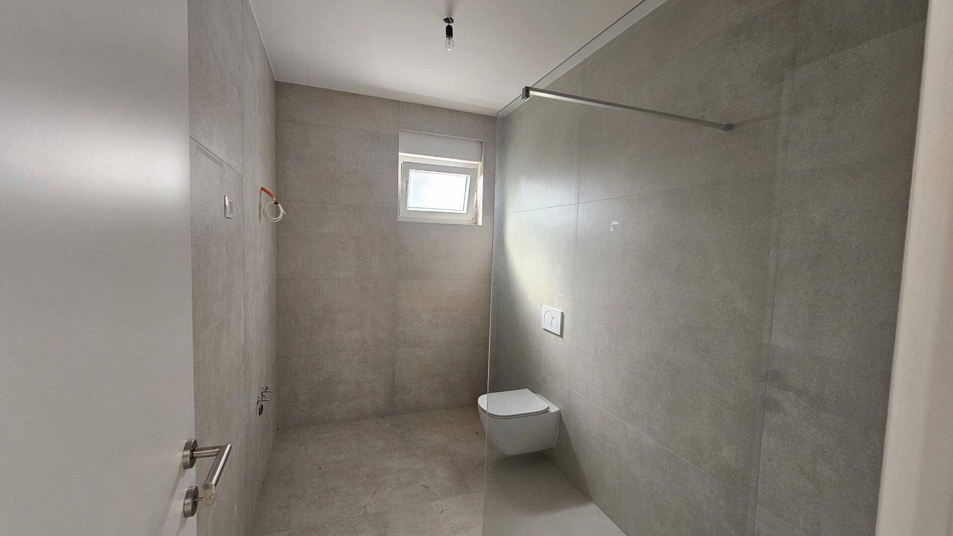 Modernes Badezimmer mit Dusche, Fliesen an Wänden und Boden sowie einem Fenster.