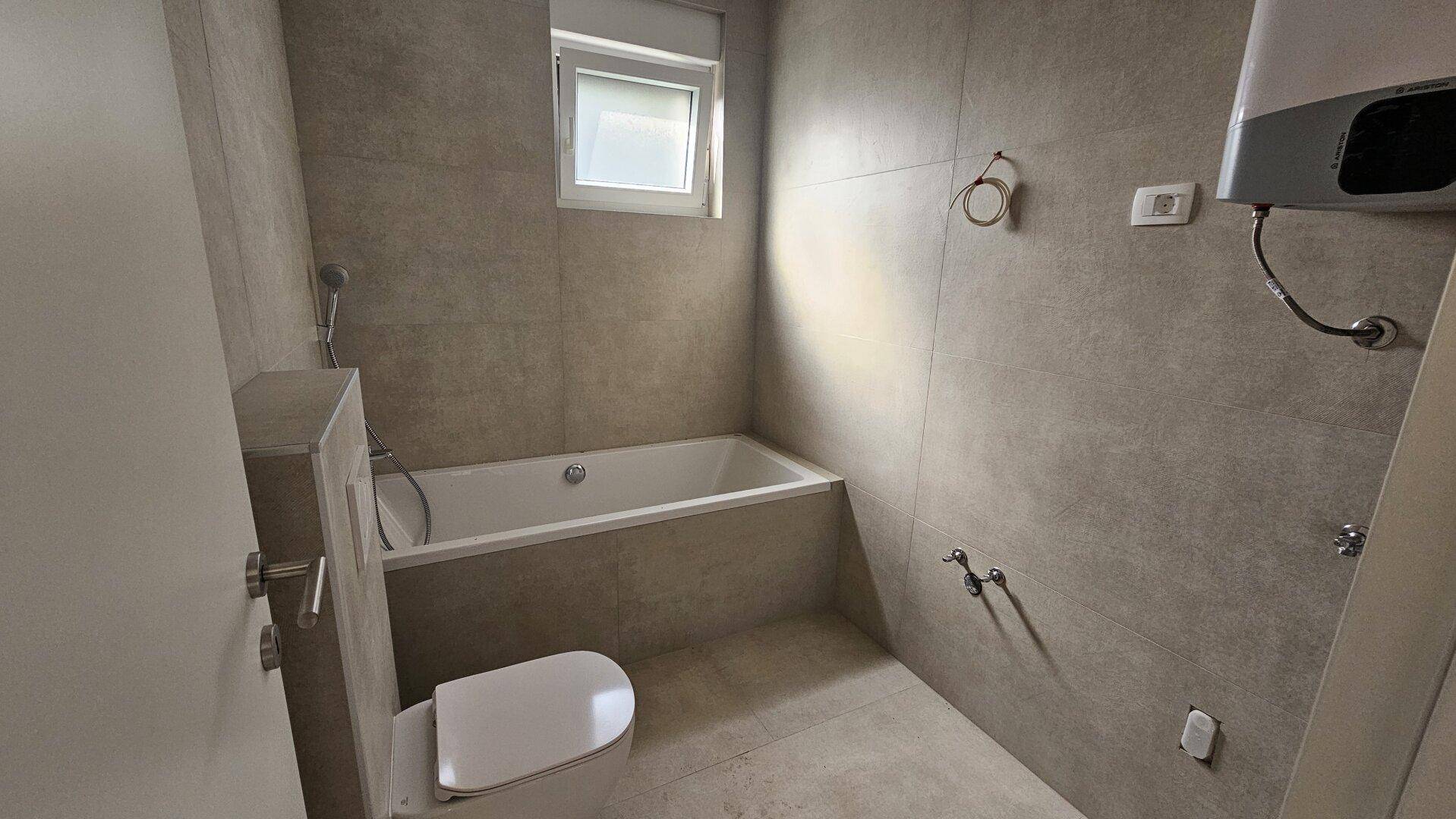 Modernes Badezimmer mit Badewanne, Fliesen an Wänden und Boden sowie einem Fenster.