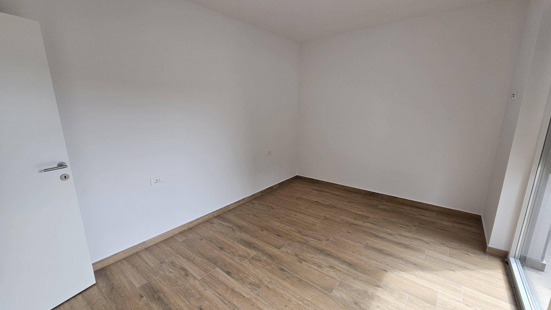 Leeres Zimmer mit Laminatboden und Zugang zu einem Außenbereich.