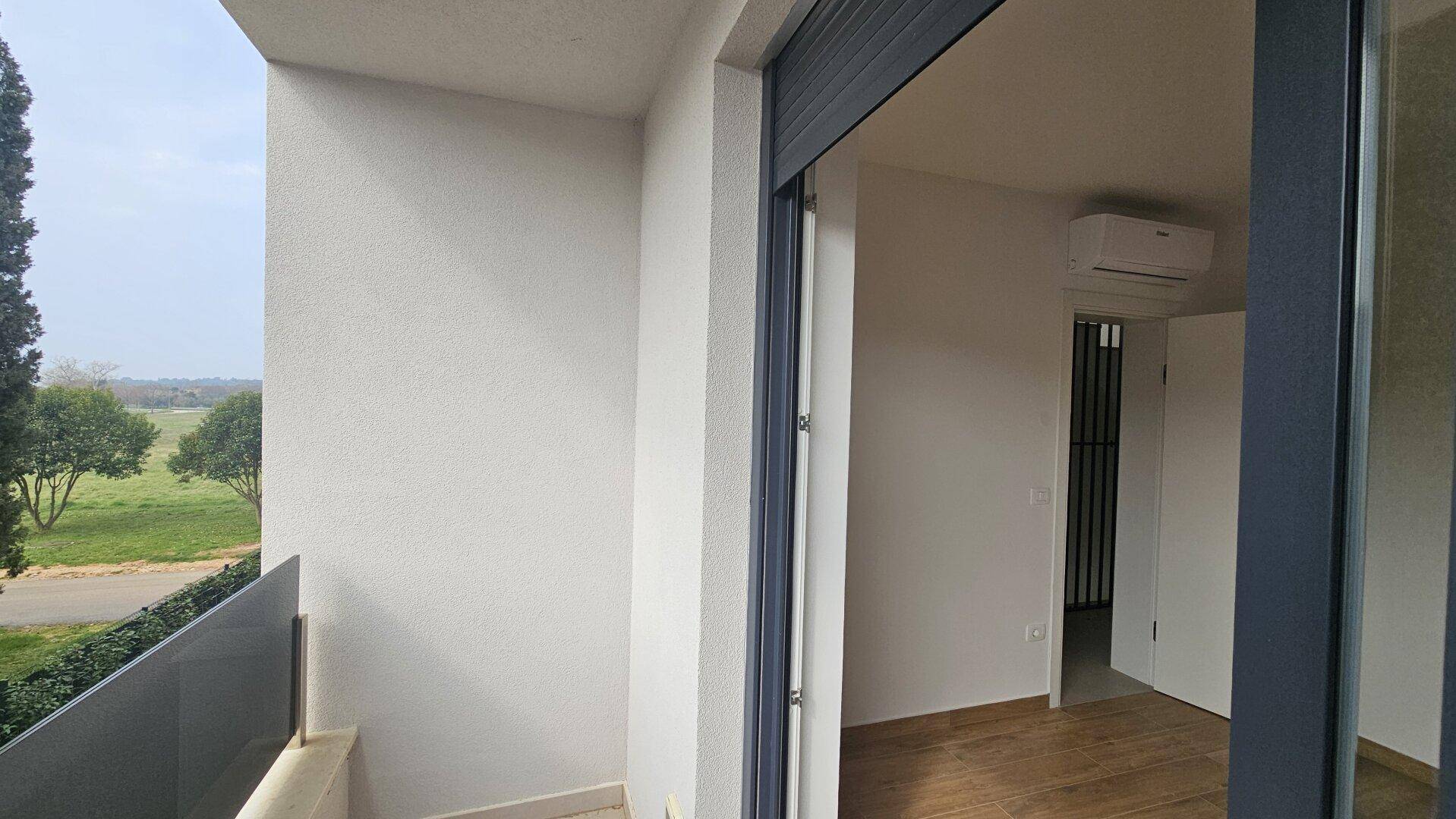 Leeres Zimmer mit Balkonzugang, Laminatboden und Blick ins Grüne.