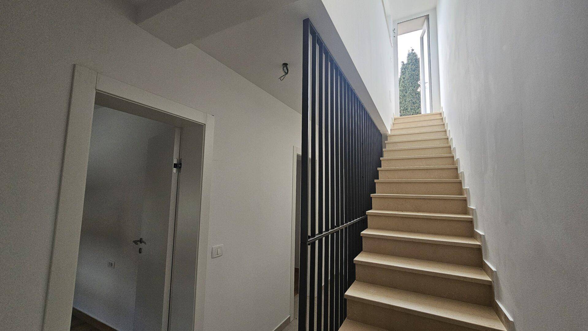 Moderne Treppe mit hellem Fliesenboden und elegantem schwarzen Geländer.