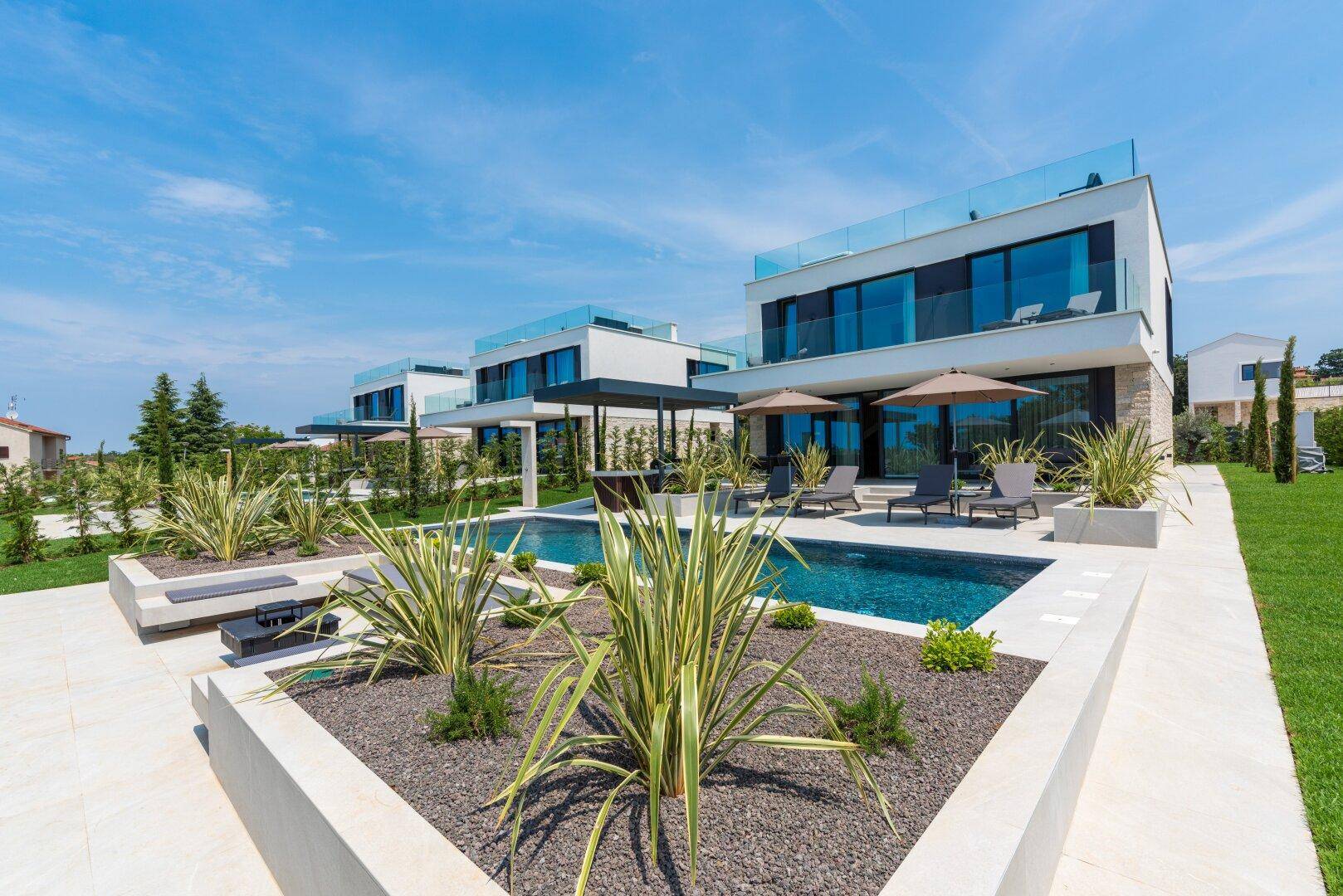 Moderne Villen mit weitläufigem Poolbereich, Sonnenterrasse und mediterraner Bepflanzung.