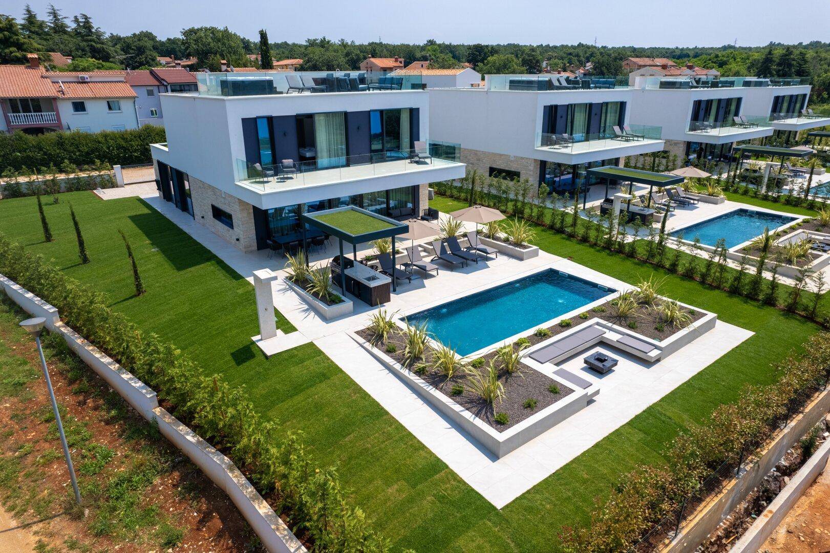 Moderne Villenanlage bei Tageslicht mit Pools, Liegebereichen und gepflegten Gärten.