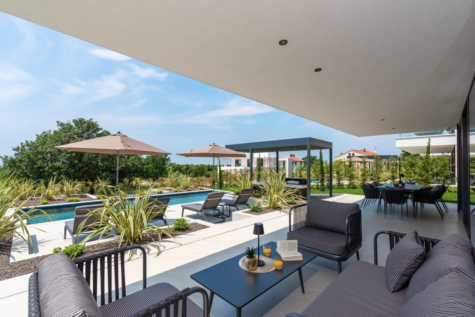Überdachte Terrasse mit stilvollen Lounge-Möbeln und Blick auf den Pool und die grüne Landschaft.