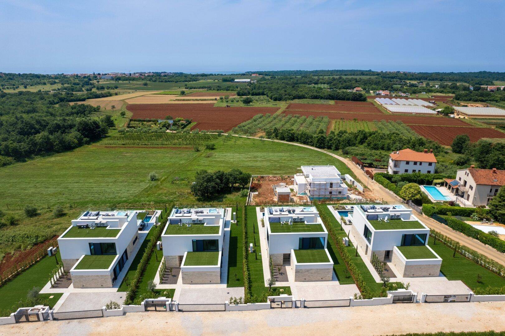 Luftaufnahme einer modernen Villenanlage mit Pools und Gärten, umgeben von Feldern und Natur.