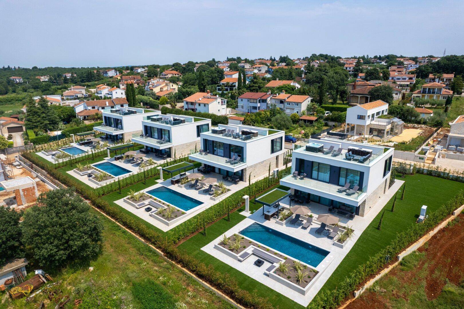 Panoramablick auf eine Reihe moderner Villen mit privaten Pools und gepflegten Außenbereichen.