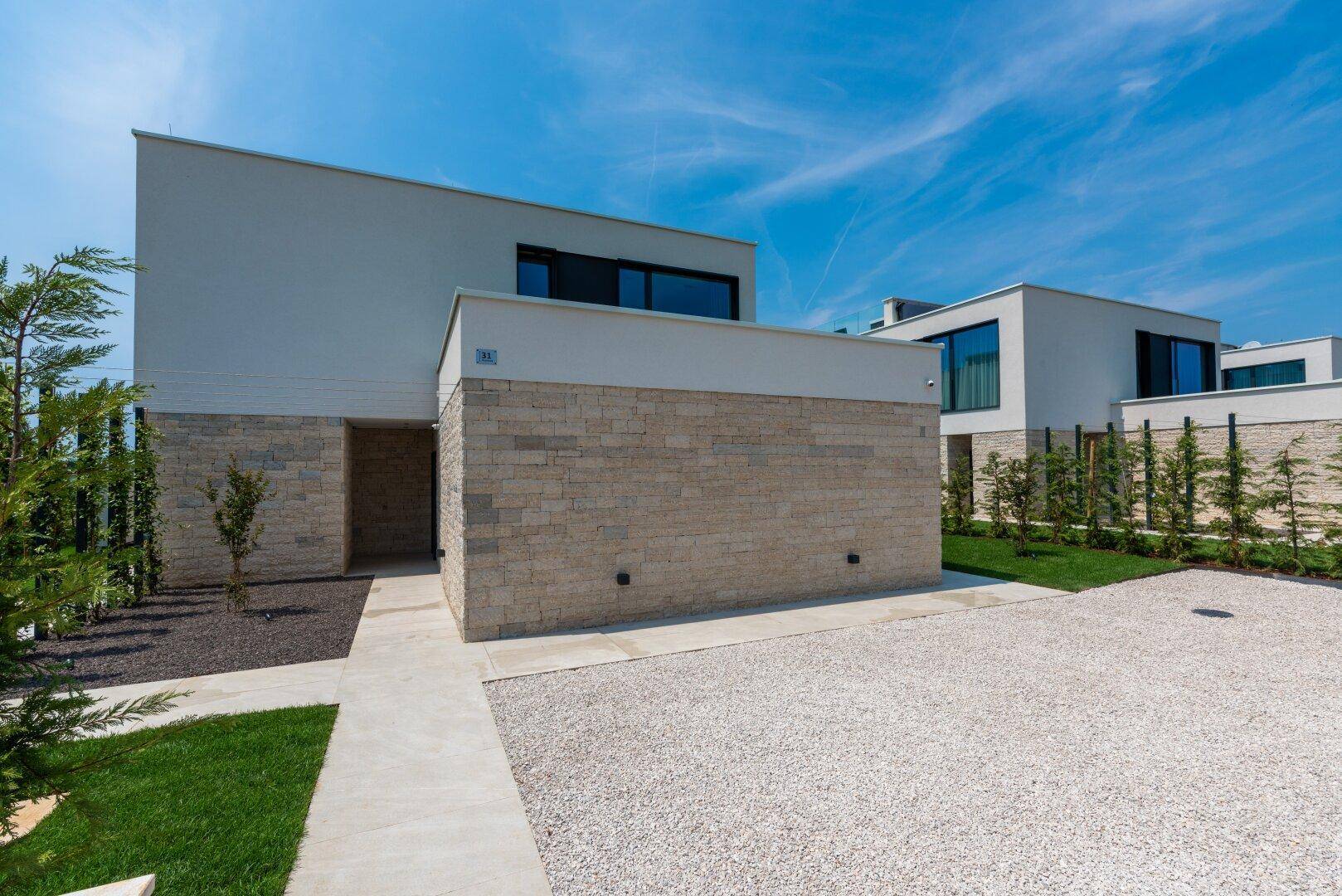Moderne Hausfassade mit Steinverkleidung und minimalistischer Gestaltung, umgeben von Grünflächen.