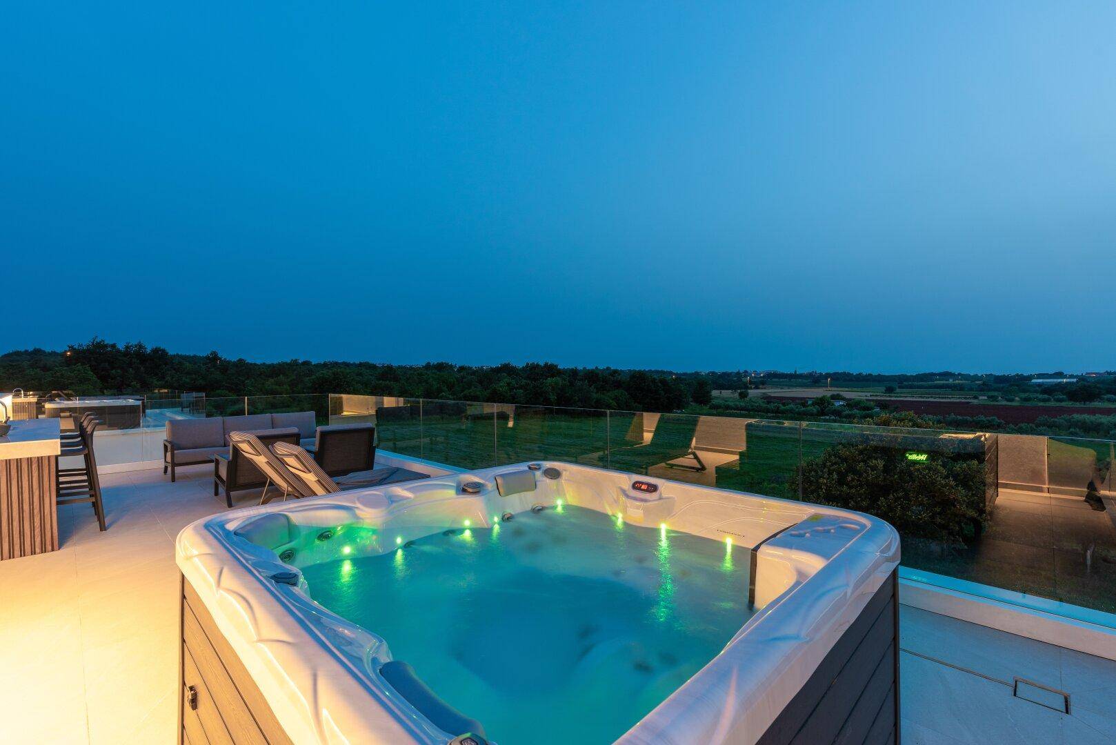 Luxuriöse Dachterrasse mit beleuchtetem Whirlpool und weitem Blick über die nächtliche Landschaft.