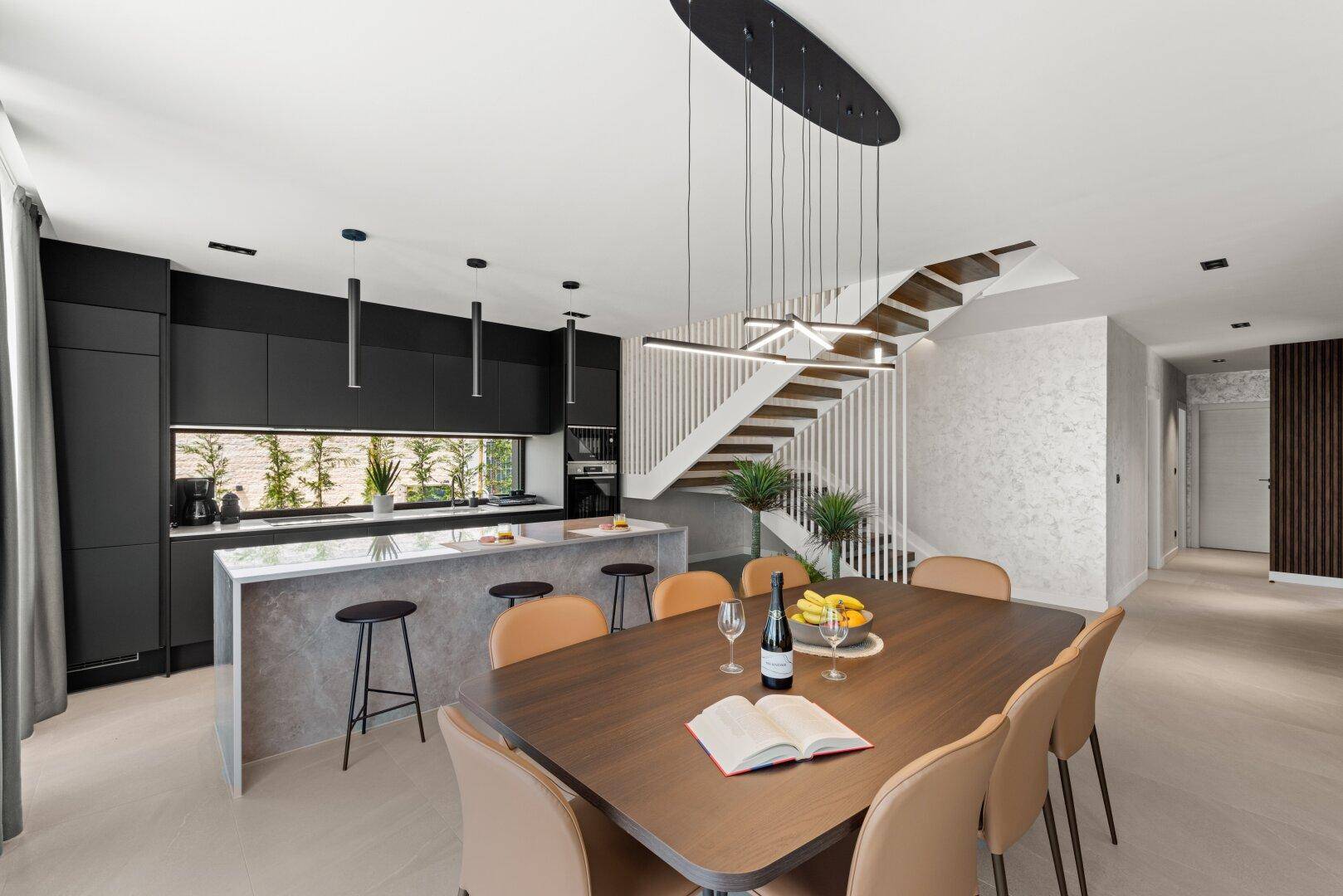 Heller Essbereich mit großem Holztisch, moderner Küche und offener Treppe zum Obergeschoss.