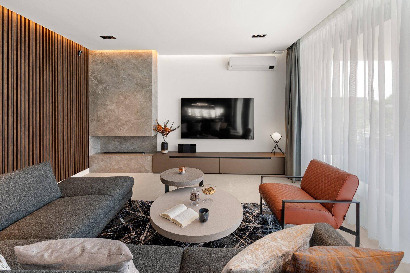 Gemütliches Wohnzimmer mit großem Sofa, Marmorakzenten und Fernseher an der Wand.