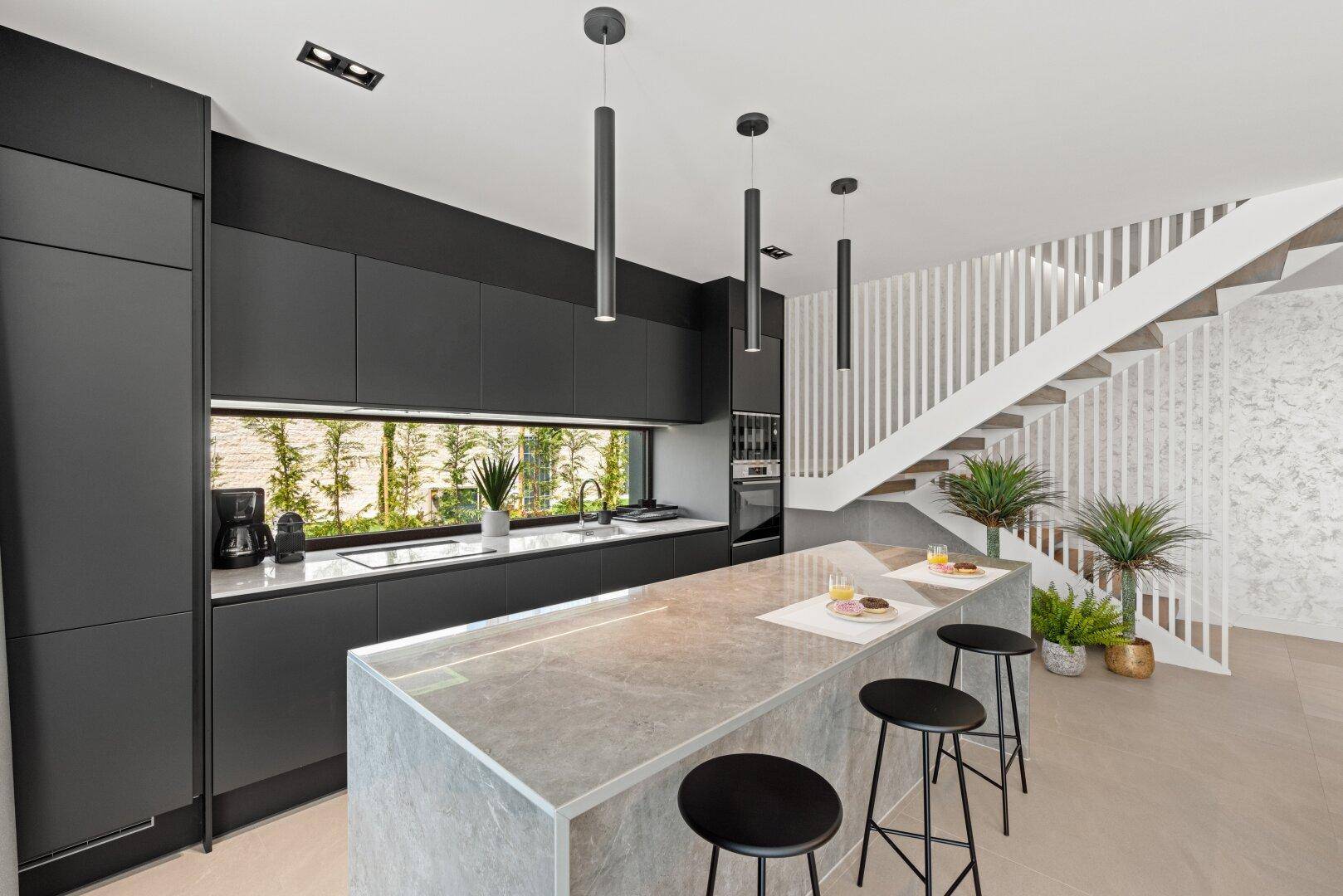 Moderne Küche mit schwarzen Schränken, Kücheninsel und offener Treppe zum Obergeschoss.