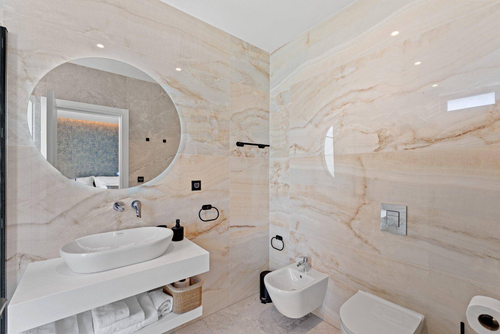 Elegantes Badezimmer mit Marmorfliesen, modernem Waschbecken und wandhängendem WC und Bidet.