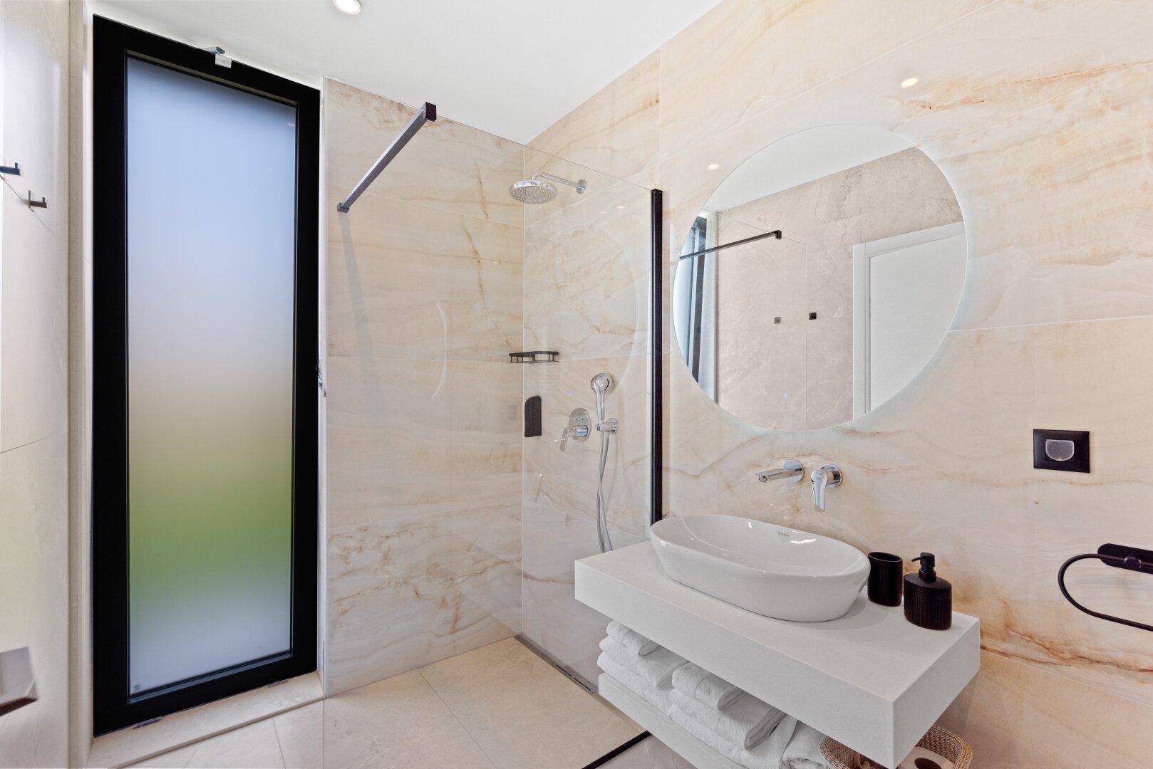 Helles Badezimmer mit Marmorfliesen, begehbarer Dusche und modernem Waschbecken.