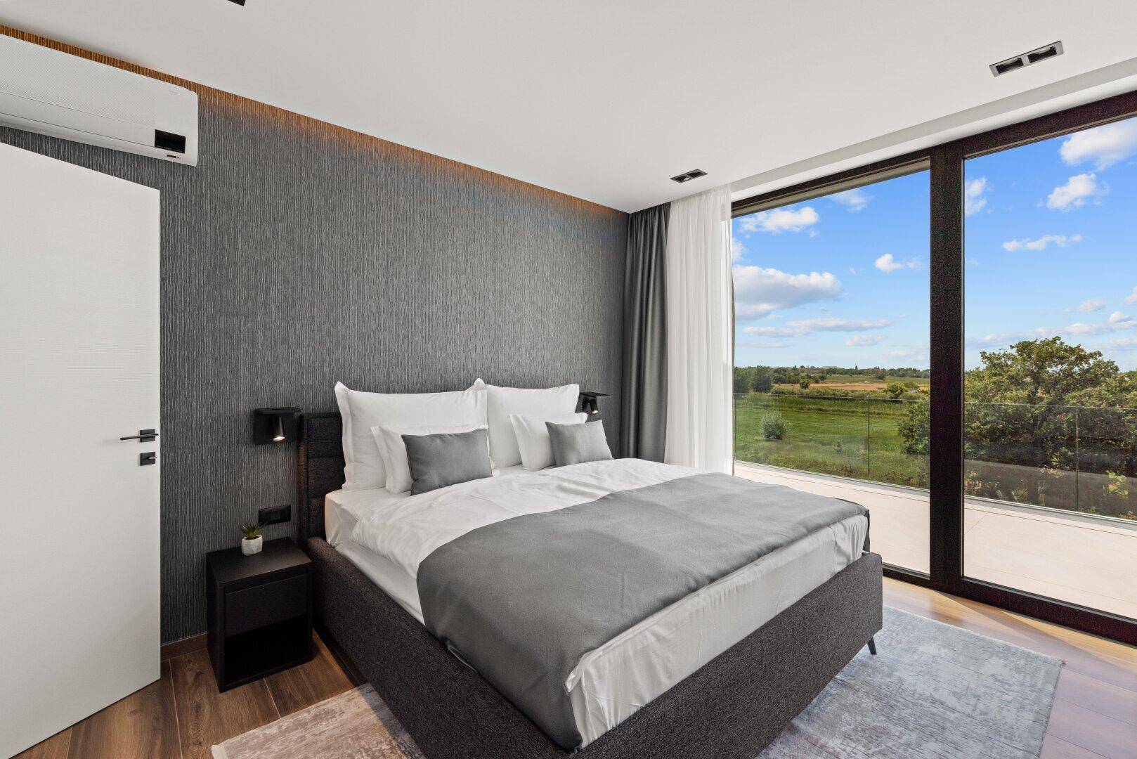 Modernes Schlafzimmer mit Doppelbett, großen Fenstern und Blick auf die grüne Landschaft.