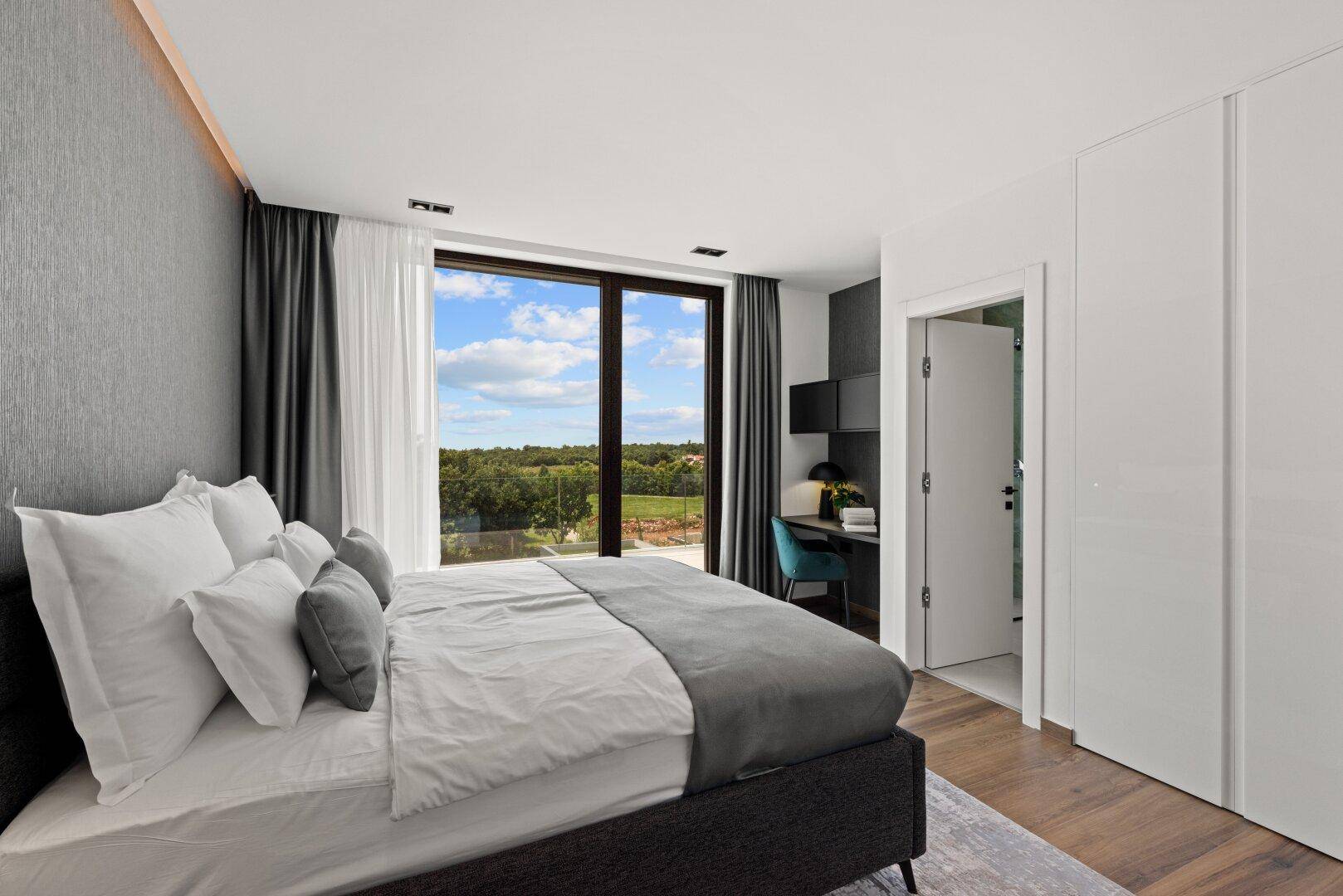 Helles Schlafzimmer mit Doppelbett, Schreibtisch und großen Fenstern mit Blick ins Grüne.