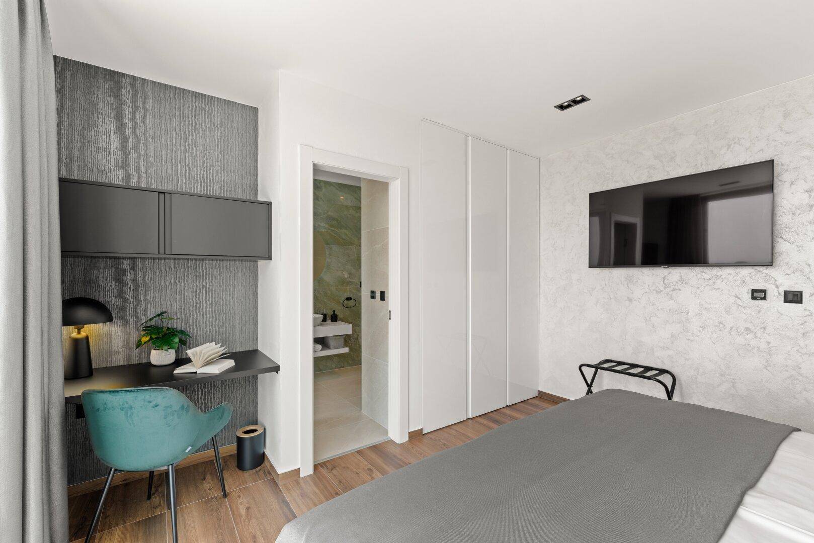 Modernes Schlafzimmer mit Doppelbett, Schreibtisch und Zugang zu einem Badezimmer.