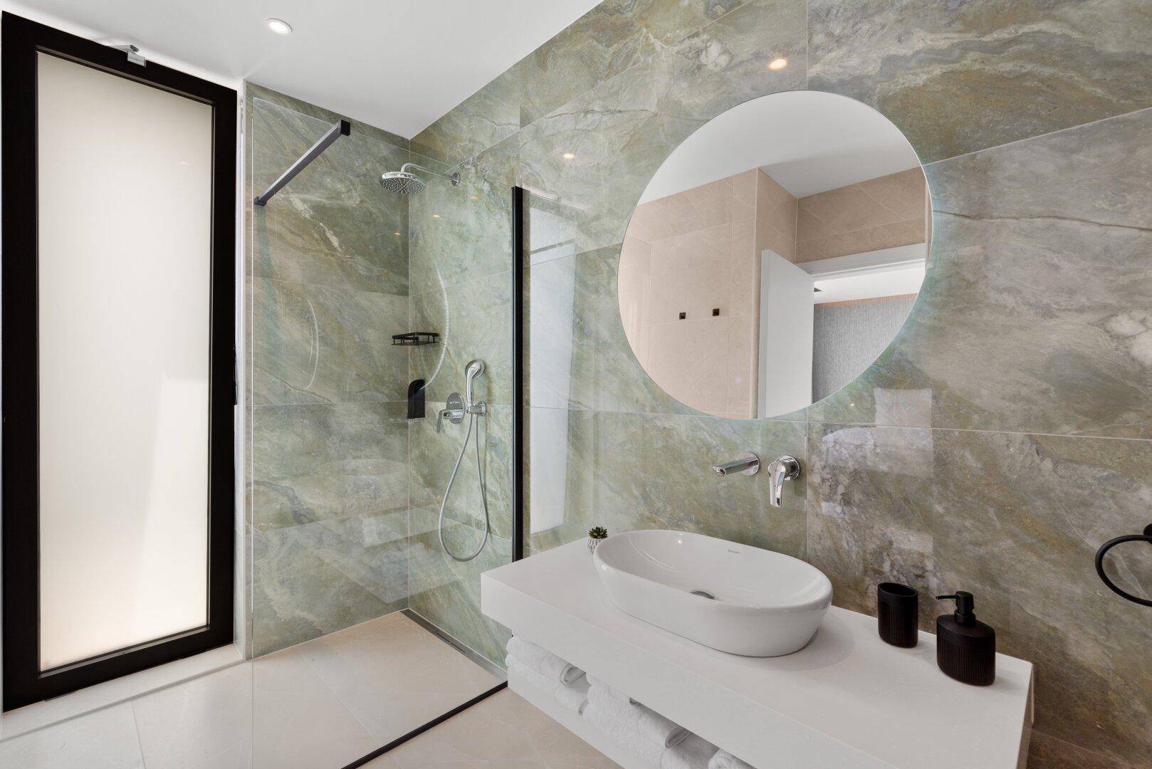Helles Badezimmer mit grünen Marmorfliesen, begehbarer Dusche und modernem Waschbecken.