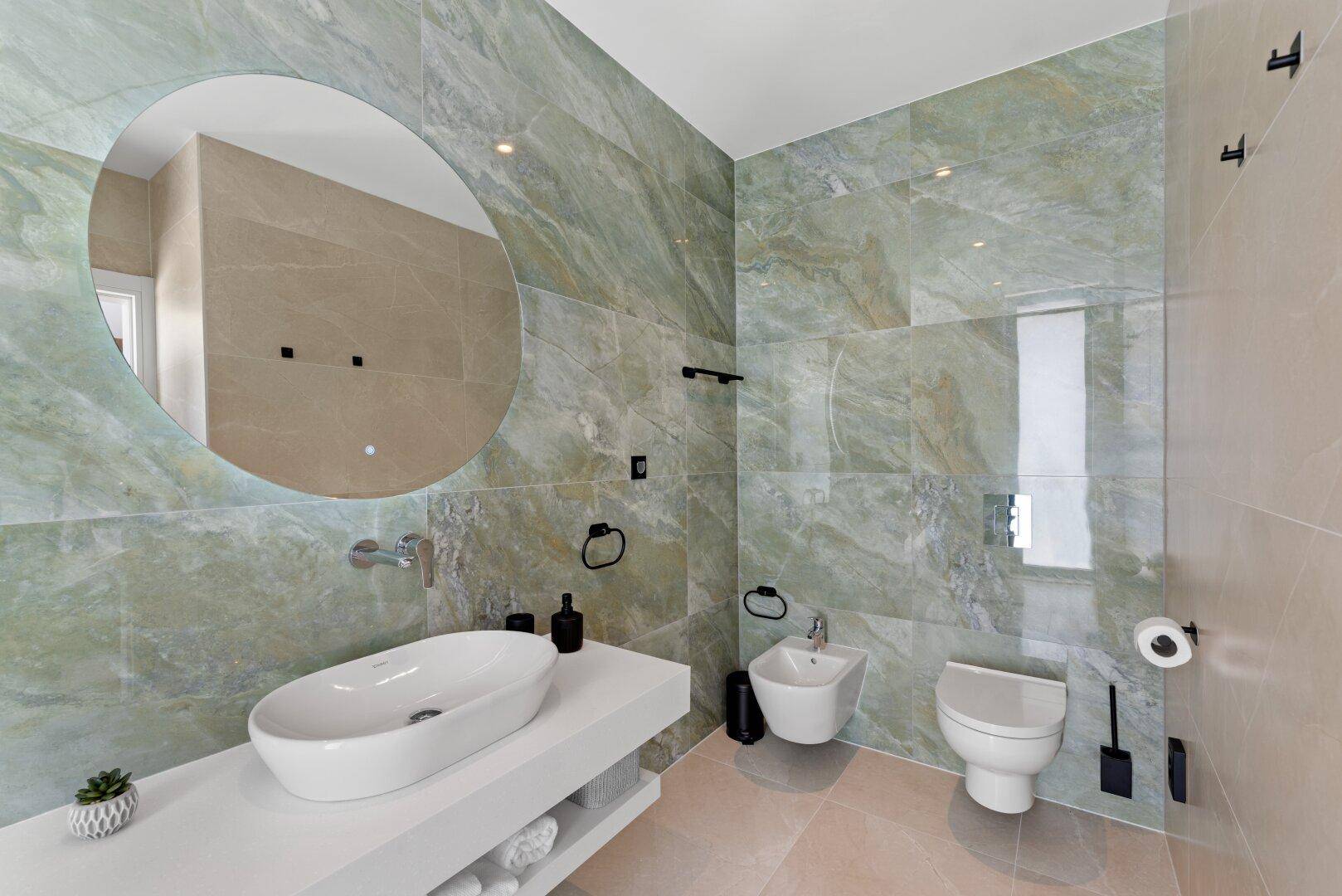 Modernes Badezimmer mit grünen Marmorfliesen, Waschbecken, wandhängendem WC und Bidet.