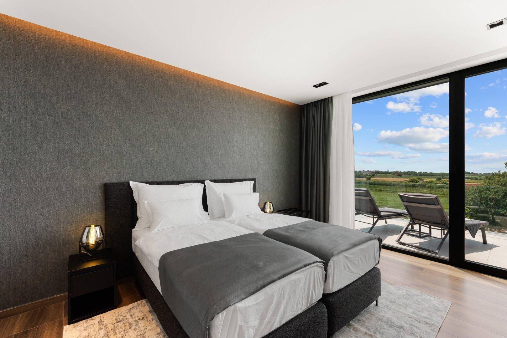 Modernes Schlafzimmer mit Doppelbett, indirekter Beleuchtung und großen Fenstern mit Landschaftsblick.