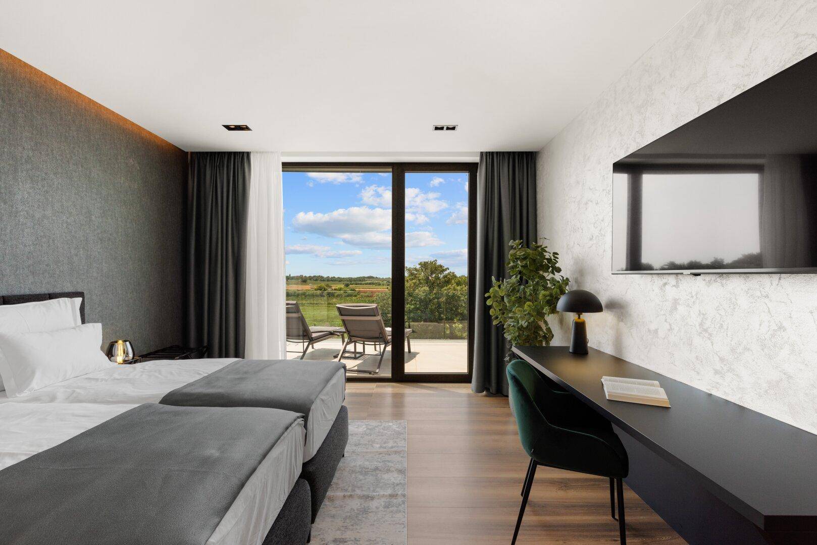 Helles Schlafzimmer mit Doppelbett, Schreibtisch und großen Fenstern mit Blick ins Grüne.