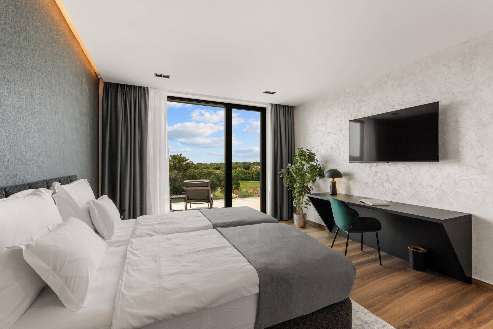 Modernes Schlafzimmer mit Doppelbett, Schreibtisch und großen Fenstern mit Blick auf die Natur.