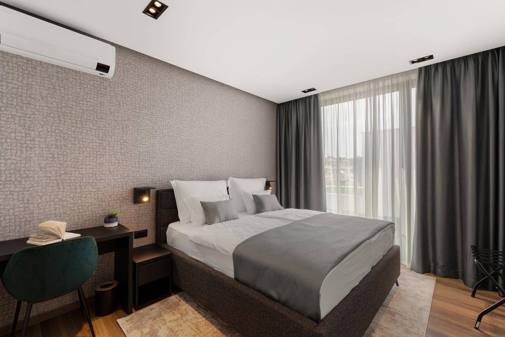 Gemütliches Schlafzimmer mit Doppelbett, Schreibtisch und großen Fenstern mit Vorhängen.