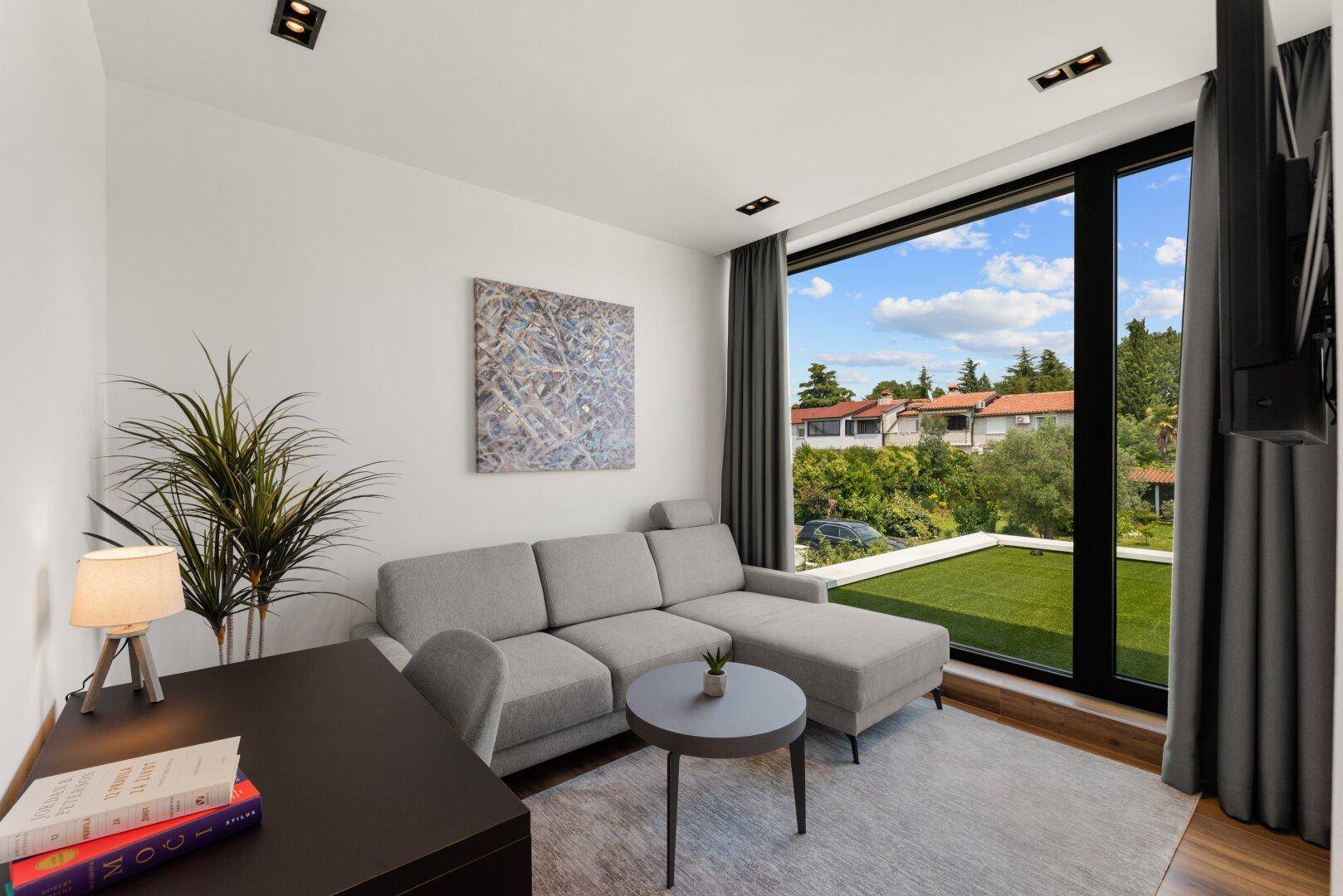 Heller Wohnbereich mit Ecksofa, Schreibtisch und großen Fenstern mit Blick auf den Garten.