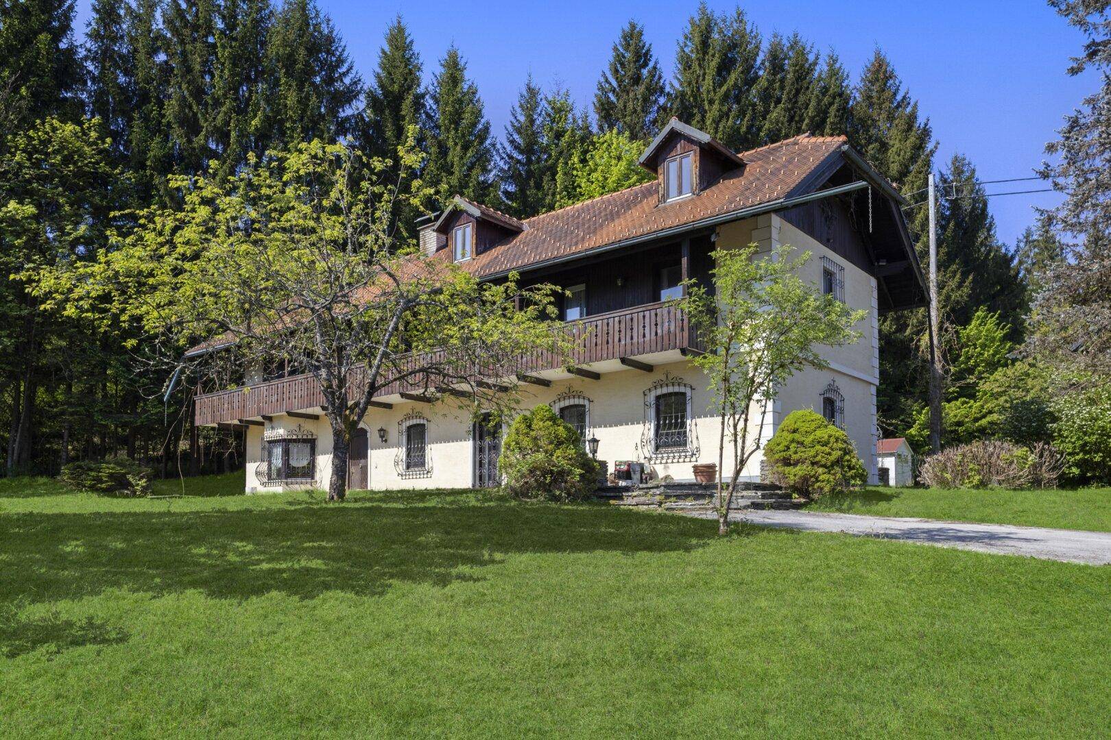 Traditionelles Landhaus mit Holzbalkonen und großem Garten, umgeben von hohen Bäumen.