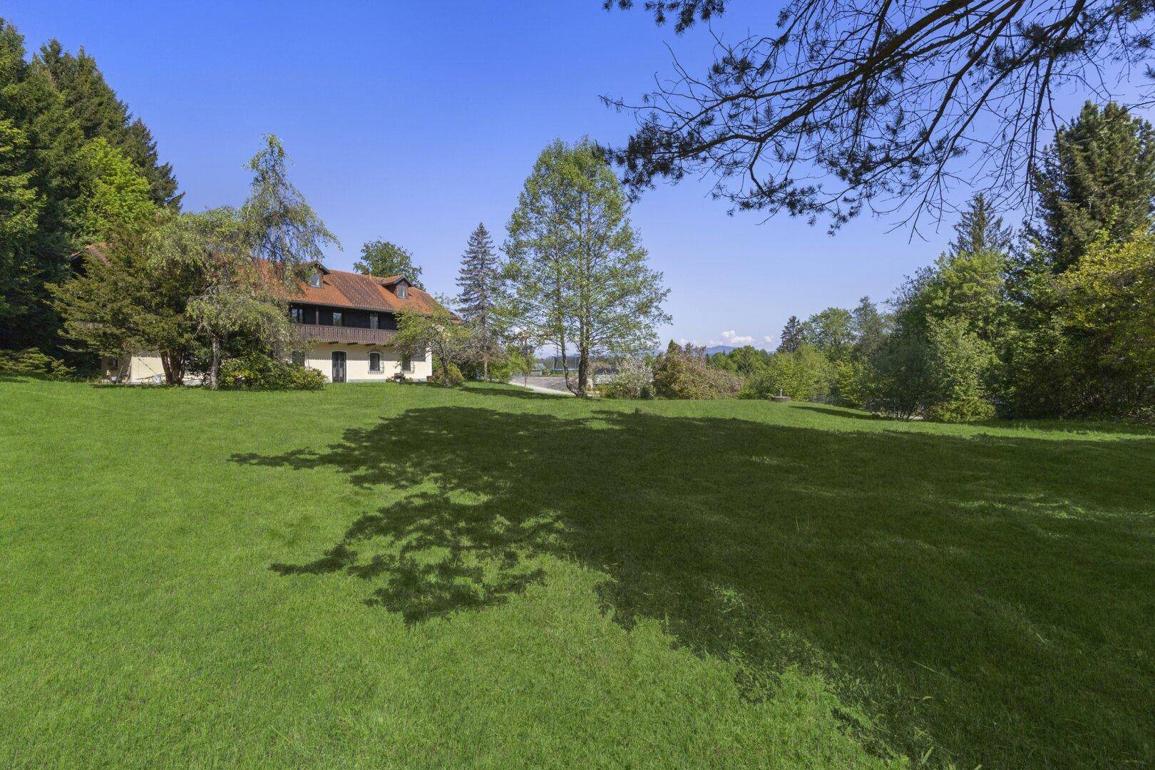 Großzügige Rasenfläche vor dem Landhaus, umgeben von üppiger Natur und Bäumen.