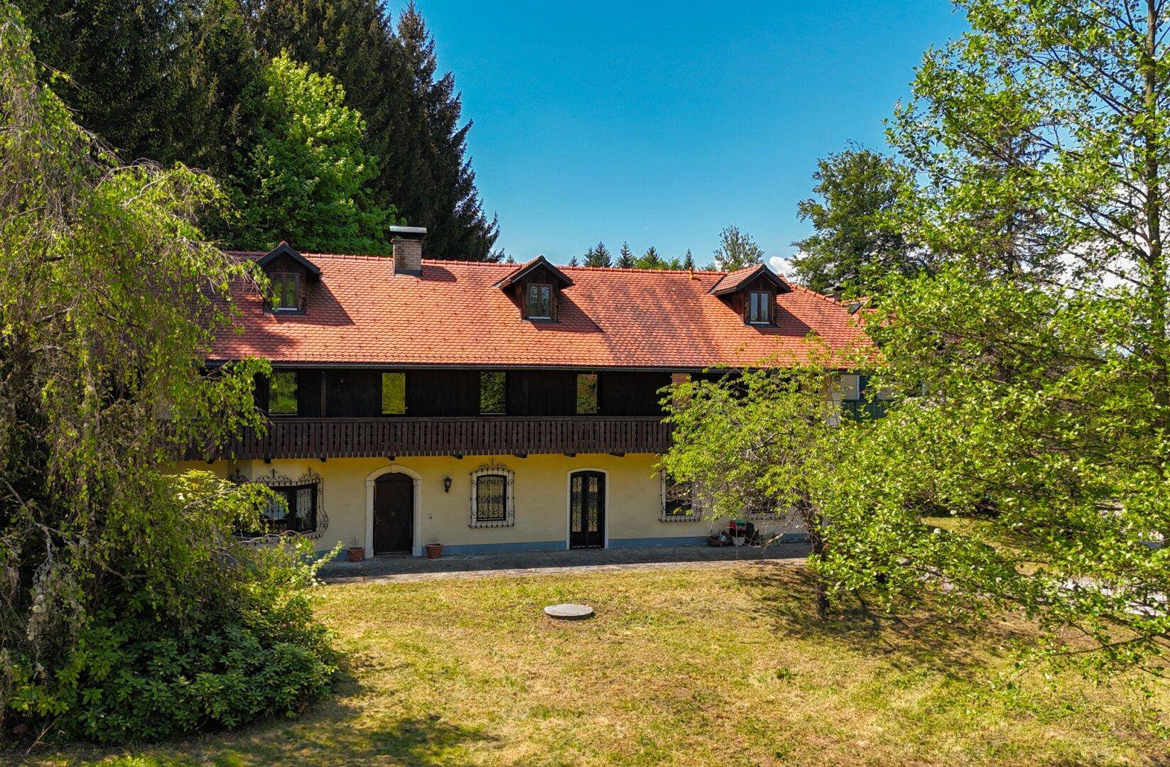 Rückansicht des Landhauses mit breitem Holzbalkon und großem, naturbelassenem Gartenbereich.