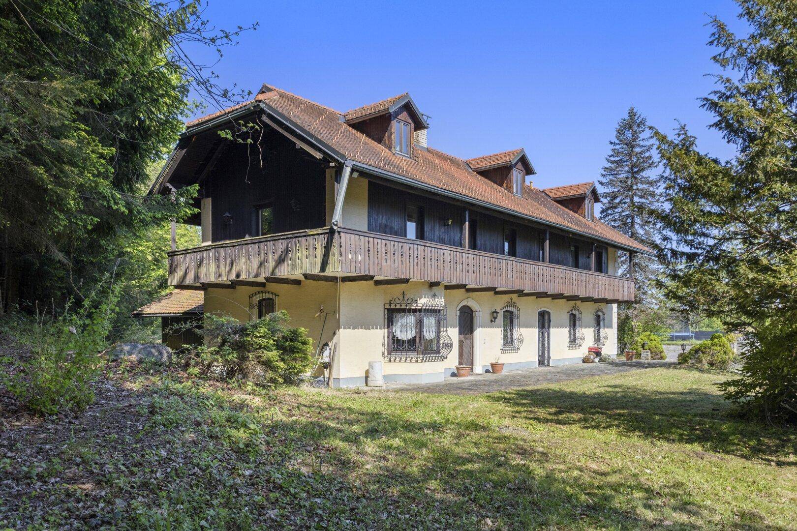 Seitliche Ansicht des Landhauses mit Holzbalkonen und Zugang zum Gartenbereich.