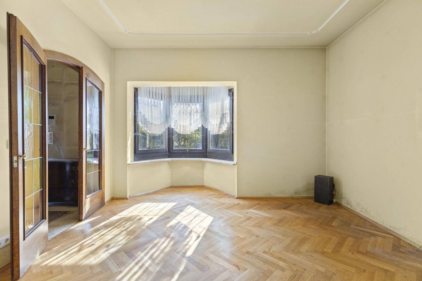 Helles Wohnzimmer mit Fischgrätparkett, Erkerfenster und Stuckdecke, bereit zur Gestaltung.