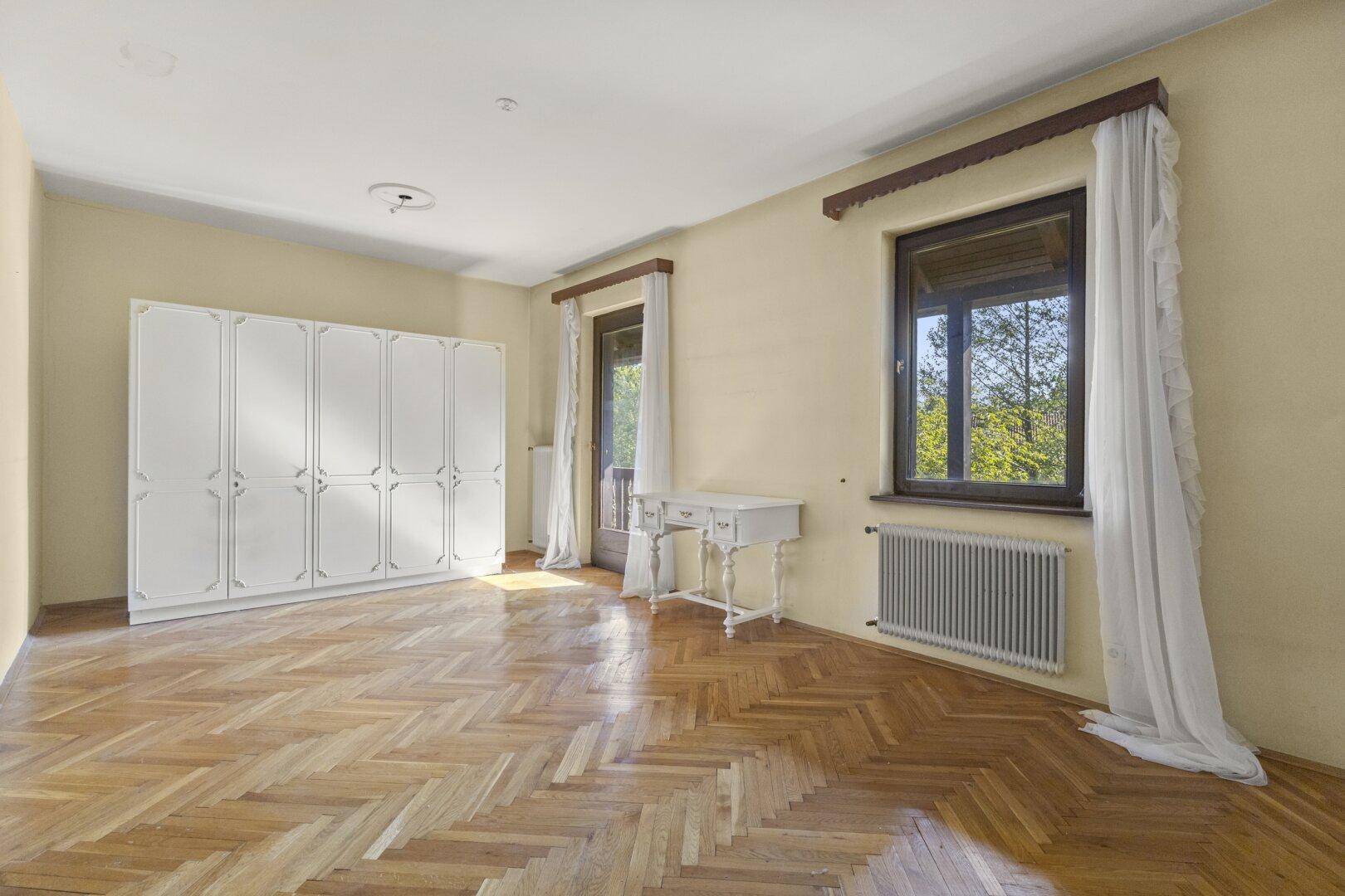 Helles Schlafzimmer mit Fischgrätparkett, großem Kleiderschrank und Zugang zum Balkon.