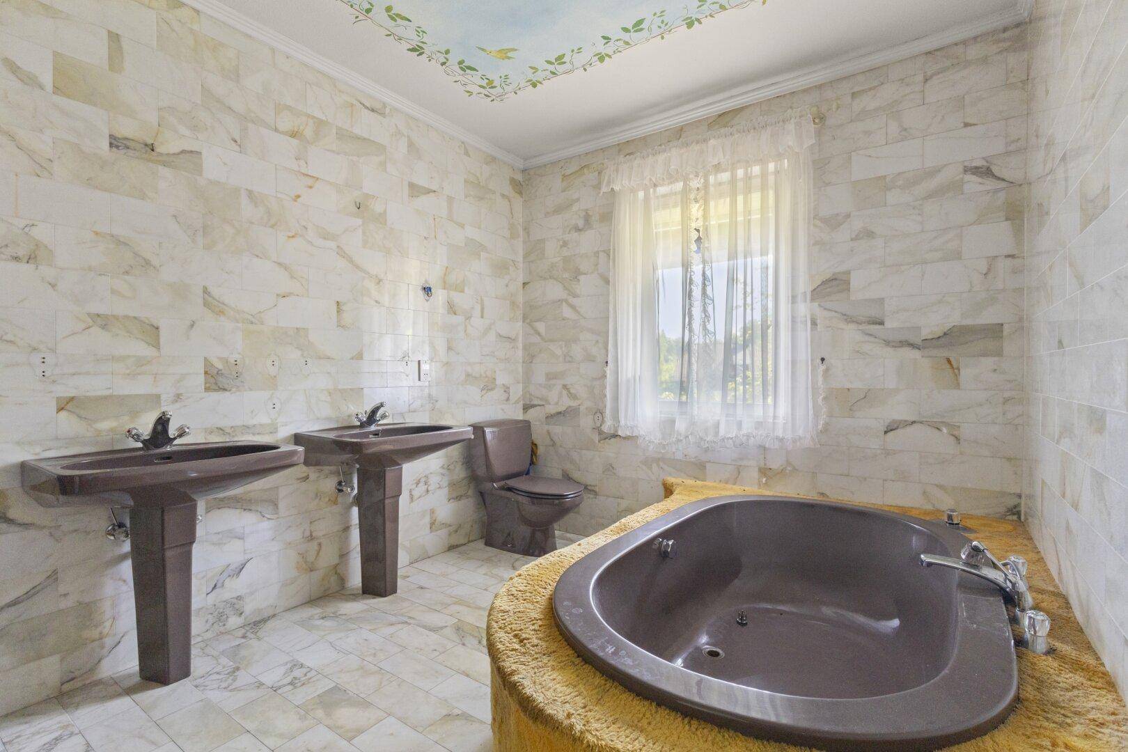 Großes Badezimmer mit doppelten Waschbecken, Badewanne und Marmorfliesen an Wänden und Boden.