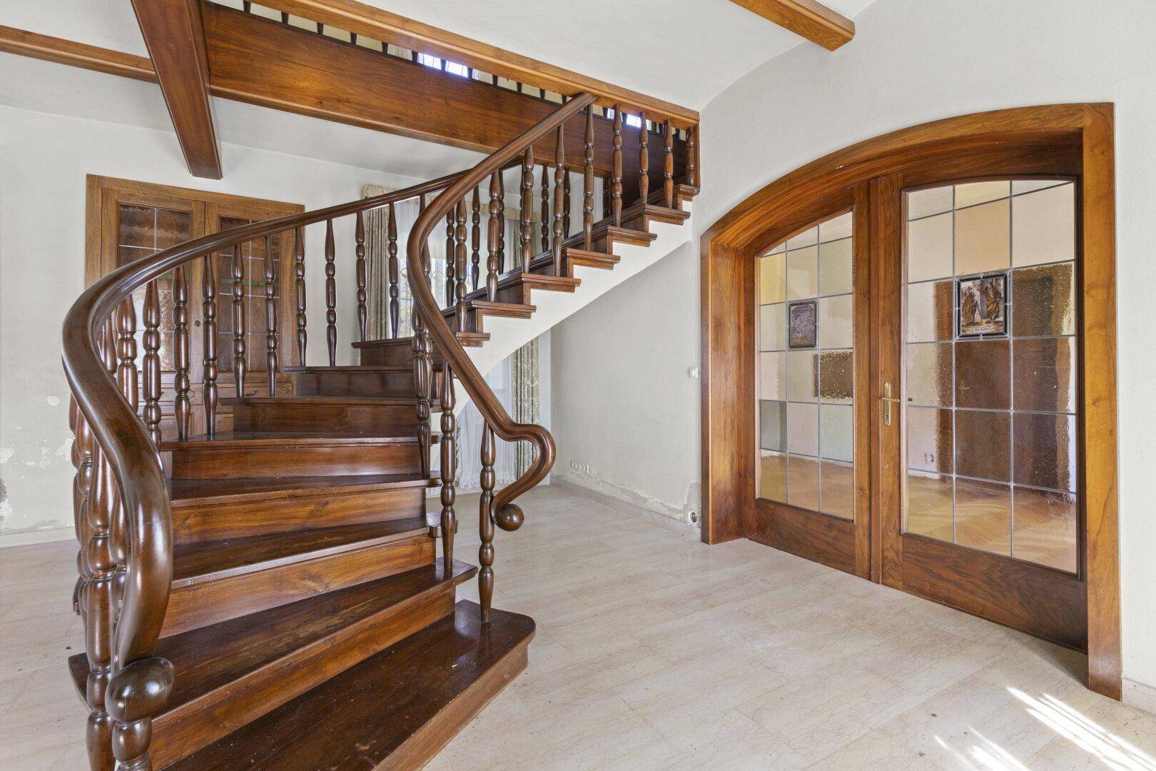 Elegante Holztreppe im Eingangsbereich mit freiliegenden Holzbalken und Marmorboden.