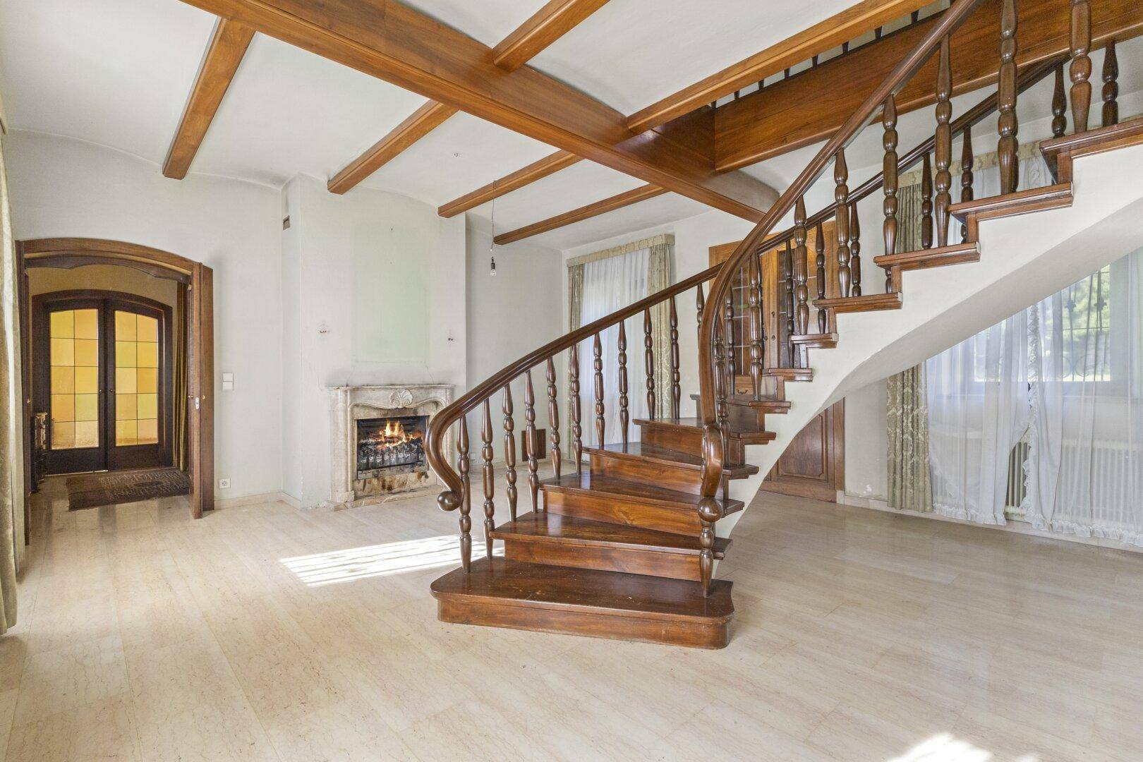 Beeindruckender Eingangsbereich mit geschwungener Holztreppe, Kamin und Marmorboden.