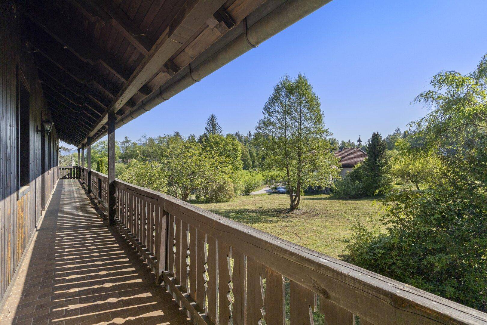 Langer Holzbalkon mit traditionellem Geländer und weitem Blick auf die grüne Landschaft.