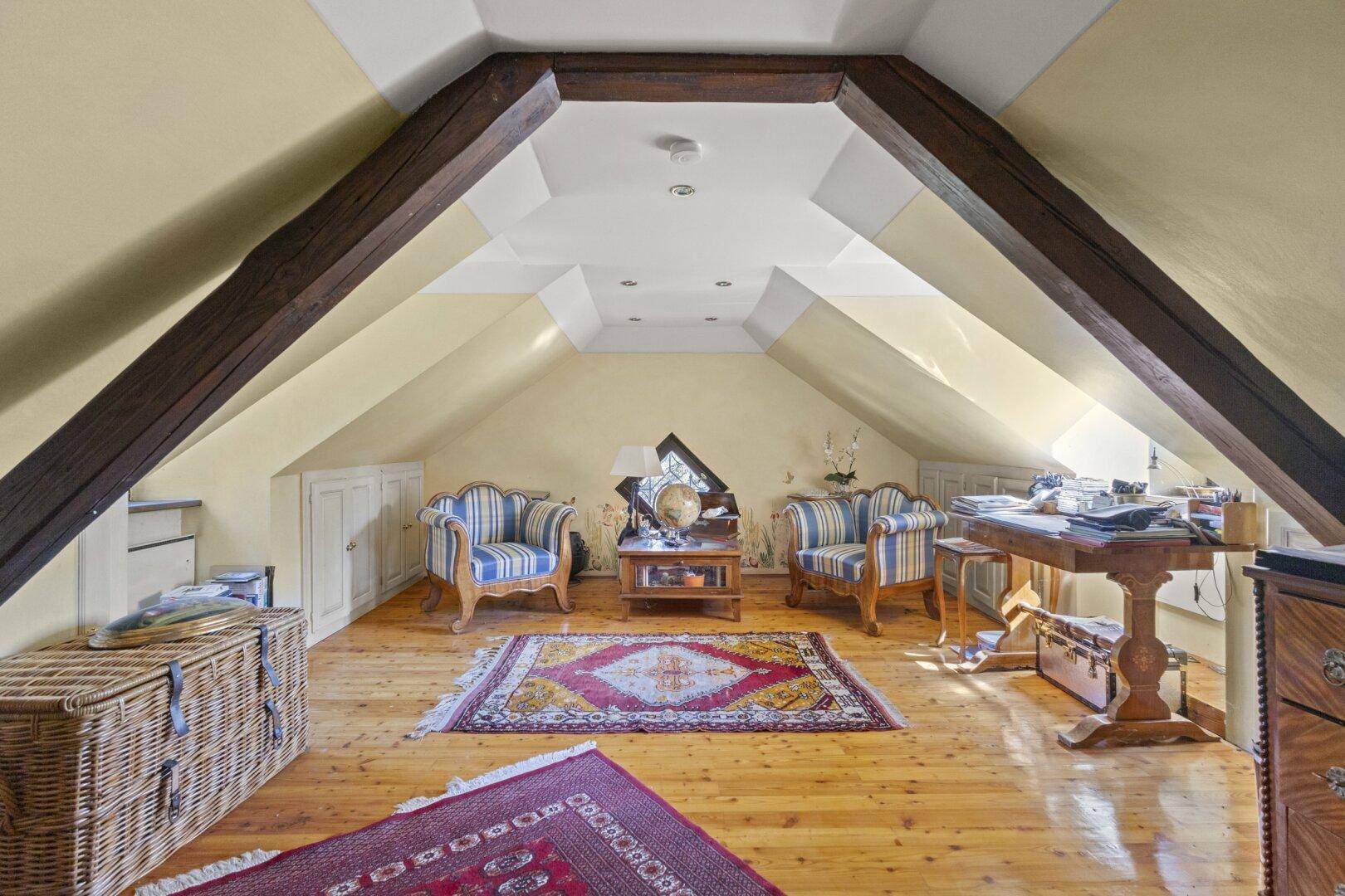 Gemütlicher Dachbodenraum mit Holzbalken, Dachschrägen und traditionellen Möbeln.