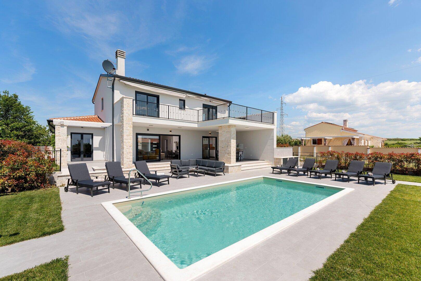 Moderne Villa mit großem Pool, Liegestühlen und Lounge-Bereich unter blauem Himmel.