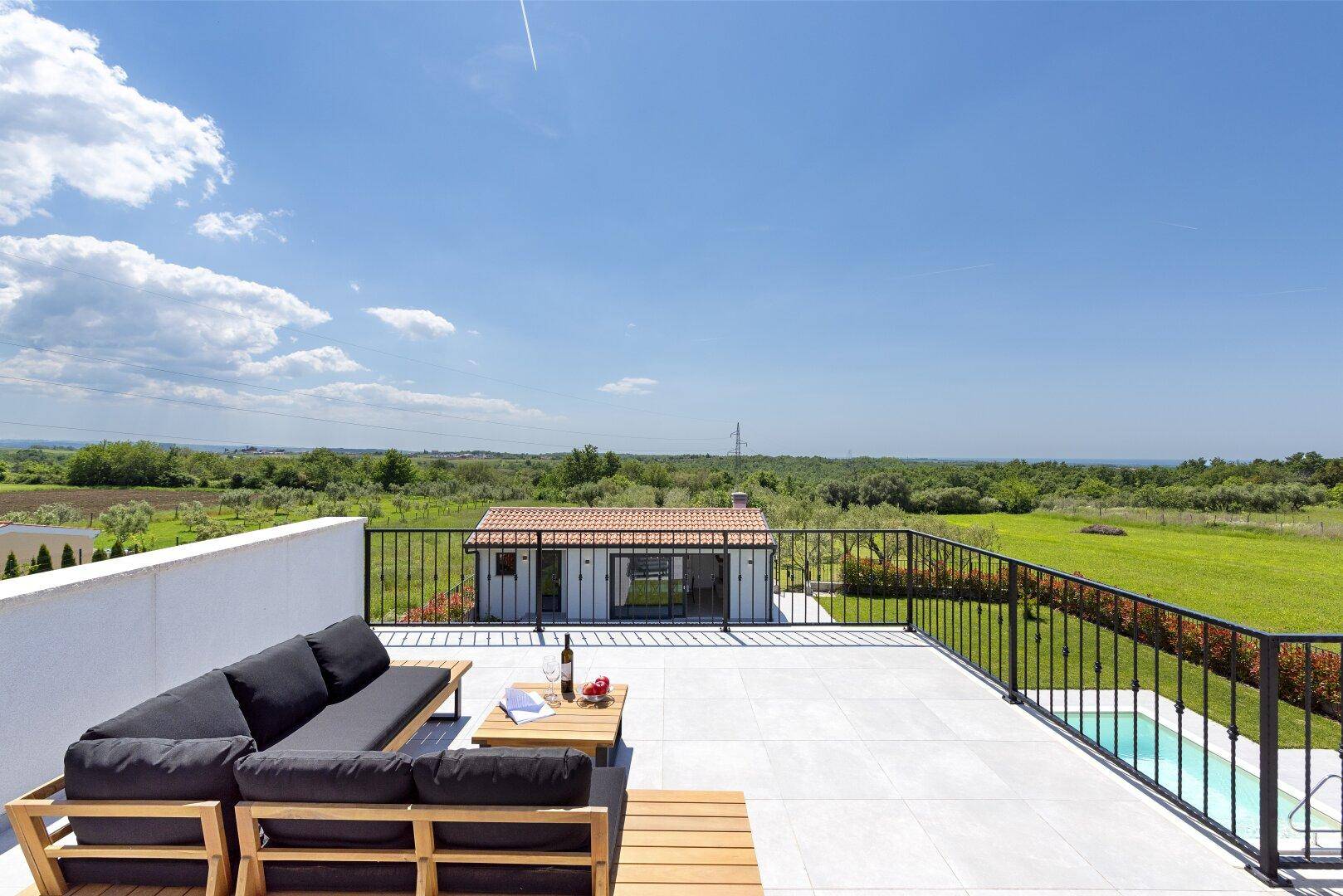 Geräumige Dachterrasse mit Lounge-Möbeln und Blick auf den Poolbereich und die grüne Umgebung.