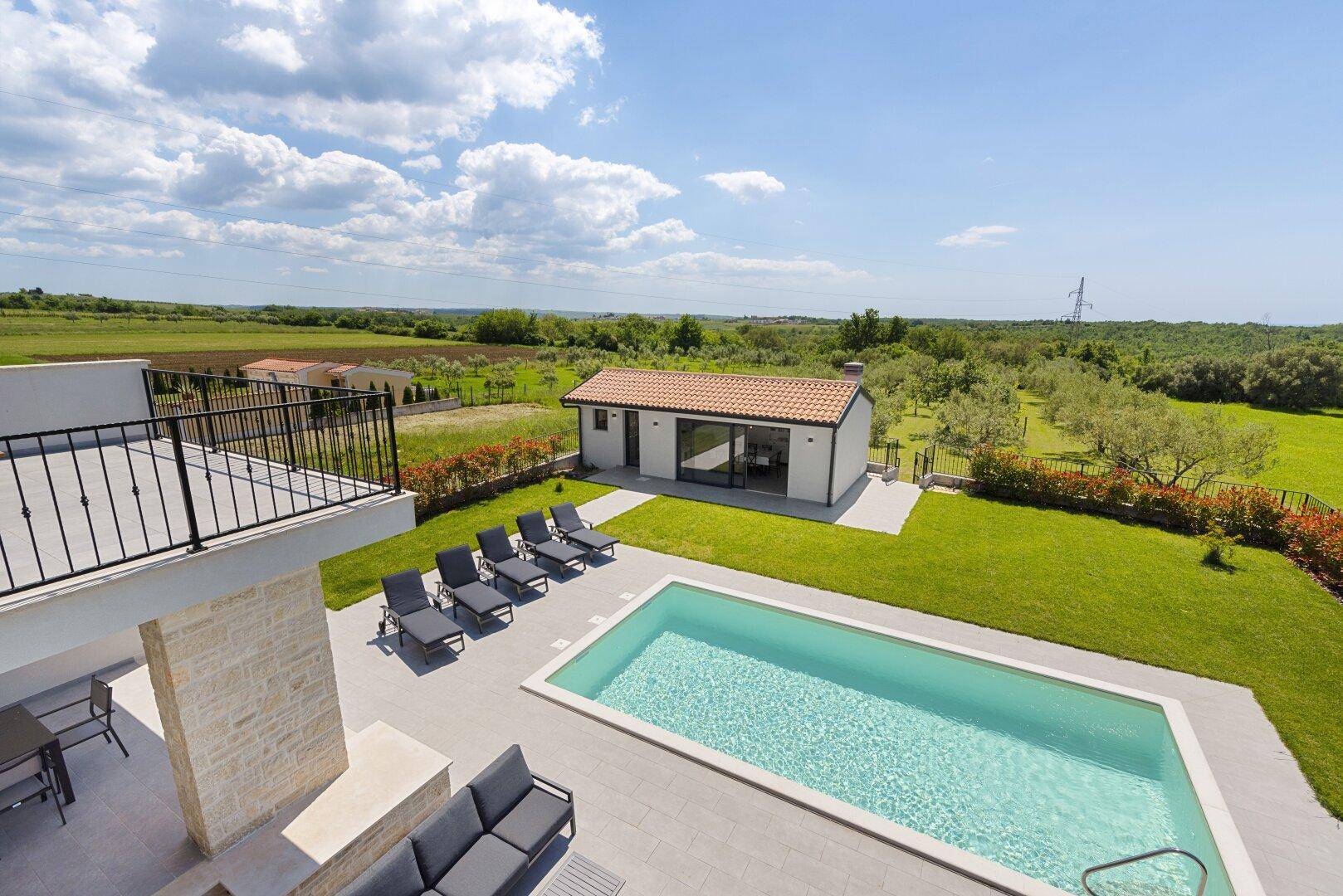 Weitläufige Außenanlage mit Pool, Hauptvilla und Nebengebäude, umgeben von grüner Landschaft.