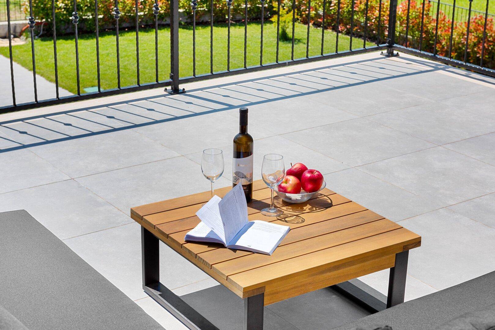 Detailaufnahme des Holztisches auf der Dachterrasse mit Wein, Gläsern und frischen Äpfeln.