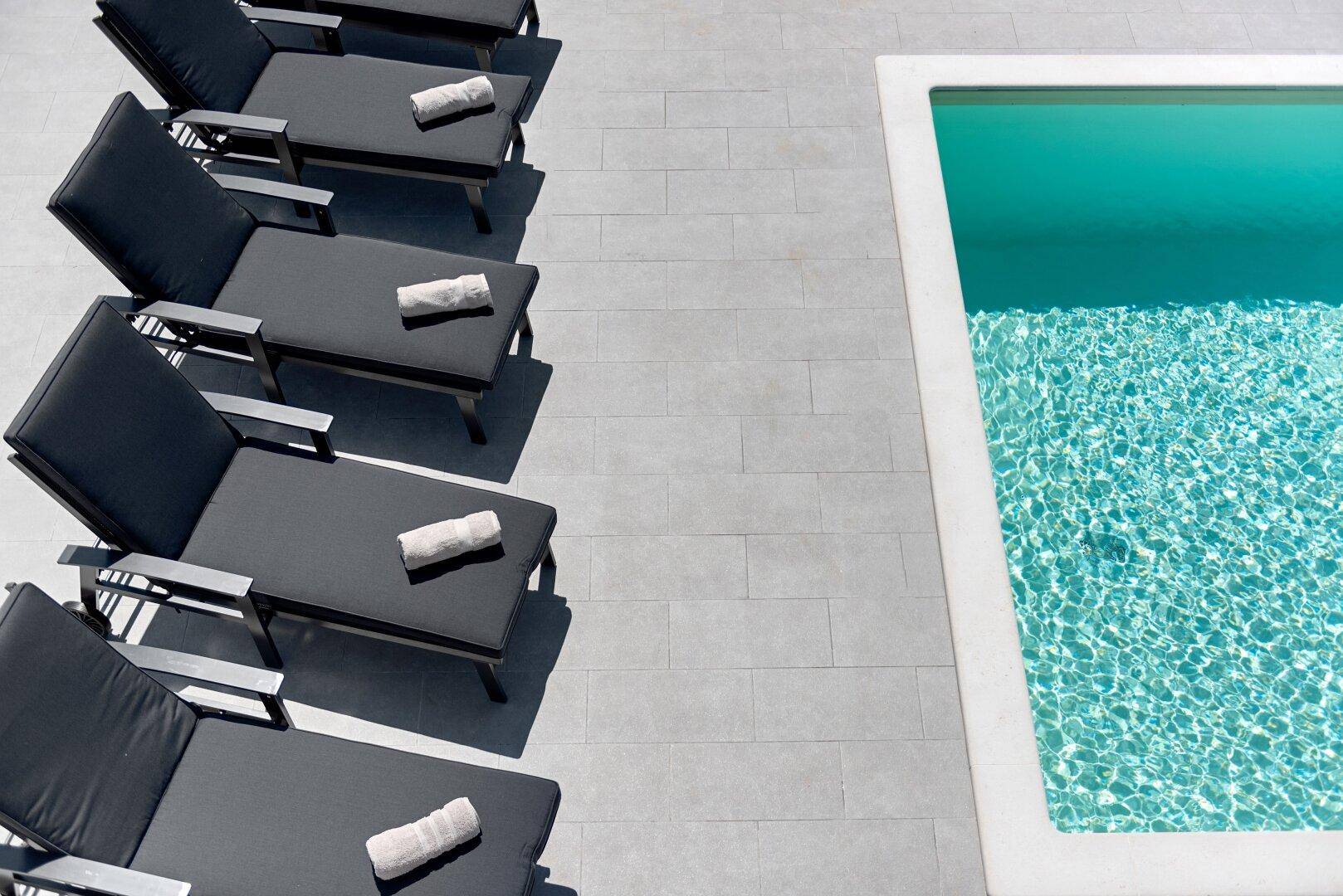 Reihe von Liegestühlen am Pool, bereit für entspannte Stunden unter der Sonne.