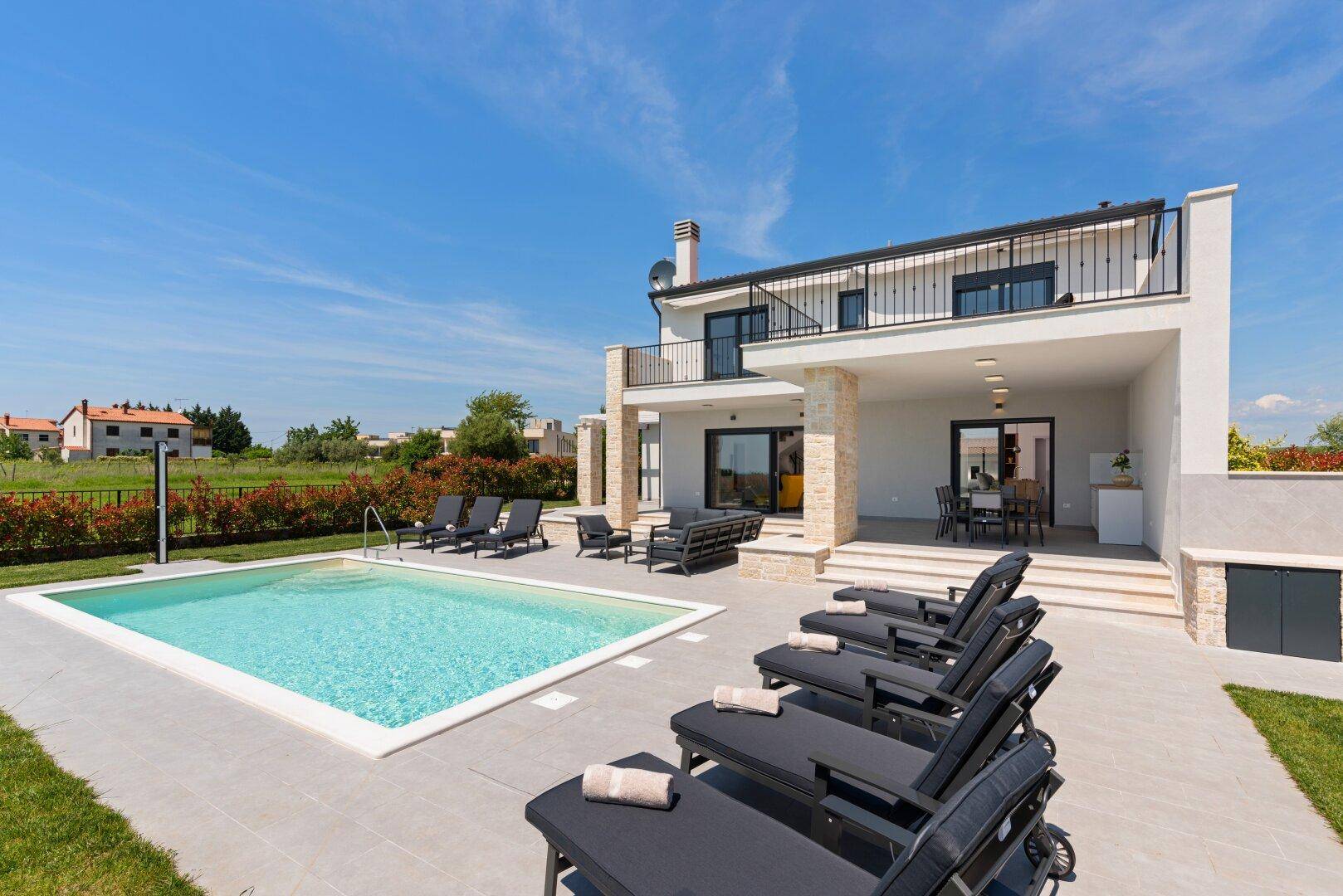 Weitläufige Poolterrasse mit zahlreichen Liegestühlen und Blick auf die moderne Villa und Landschaft.